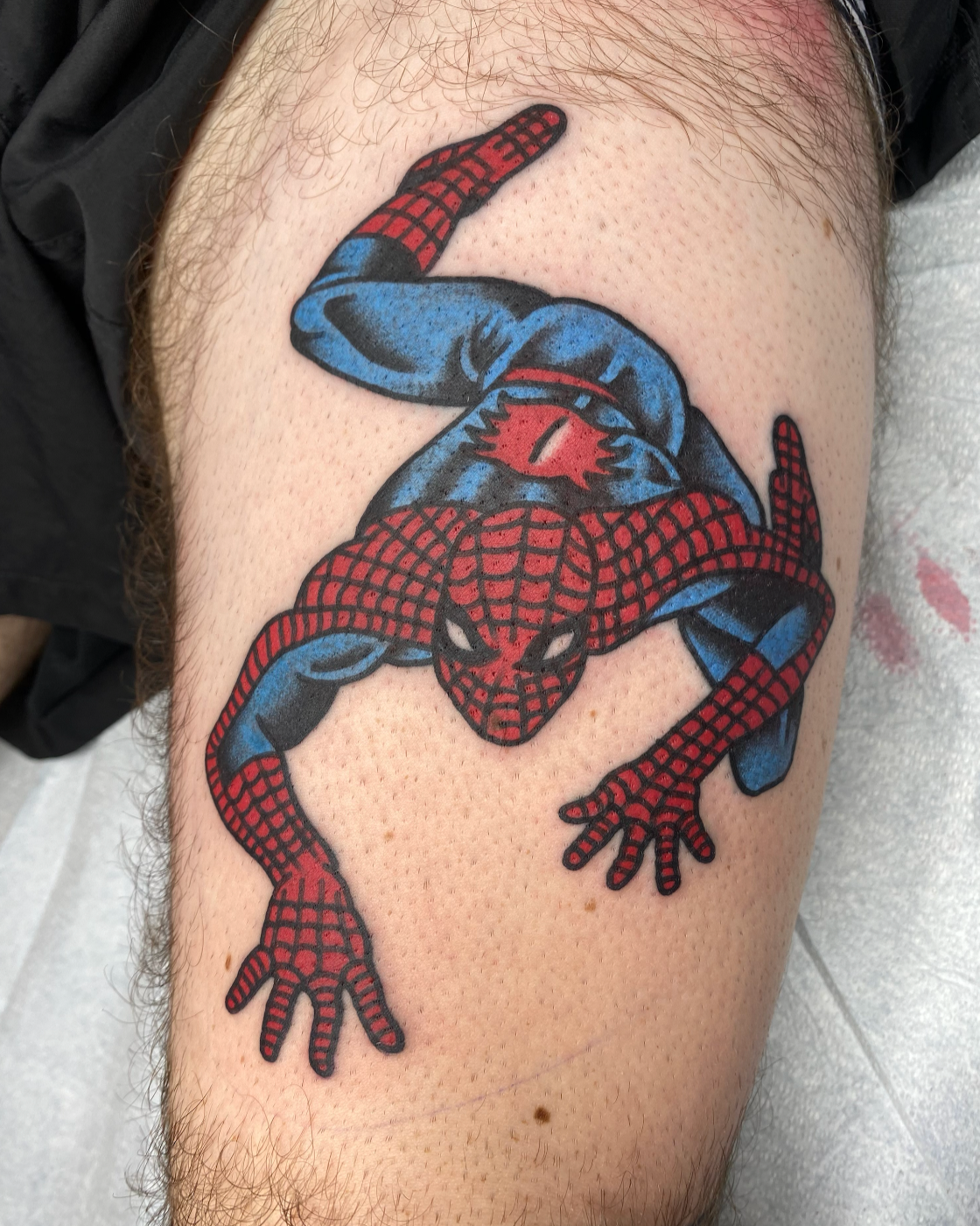 Colorful tattoo of Spider-Man in a crouching position on a person's thigh.