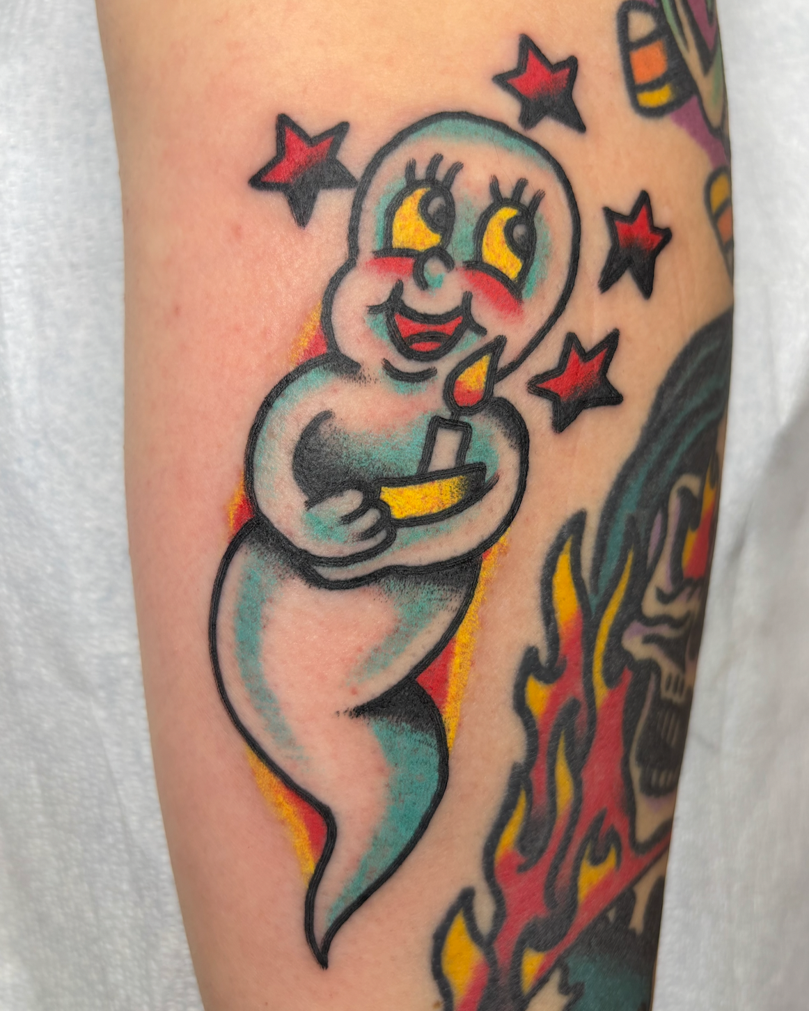 Colorful tattoo of a smiling ghost holding a lit candle, surrounded by red and black stars.