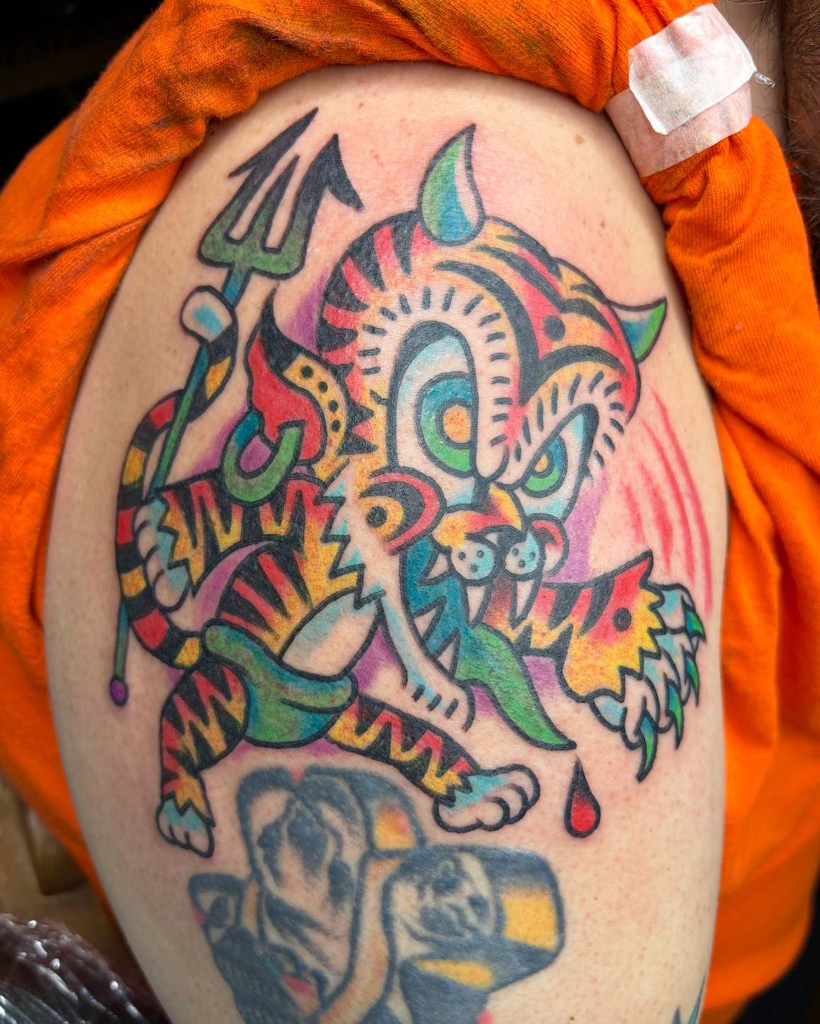 Colorful tattoo of a dragon on person's upper arm, with various vibrant colors and bold outlines.