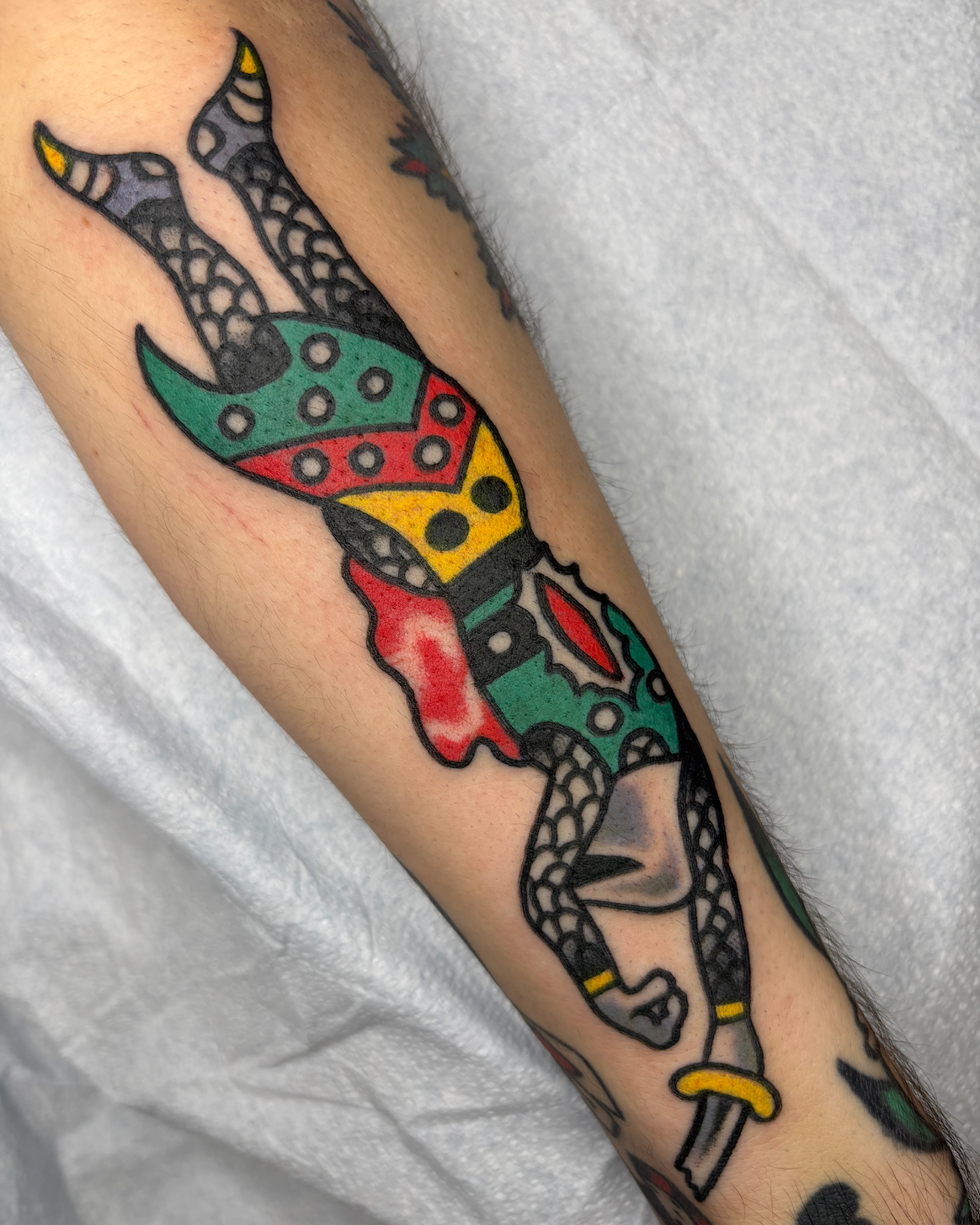 Tattoo of a colorful, stylized butterfly with black outlines and geometric patterns on the wings, on a person's forearm.