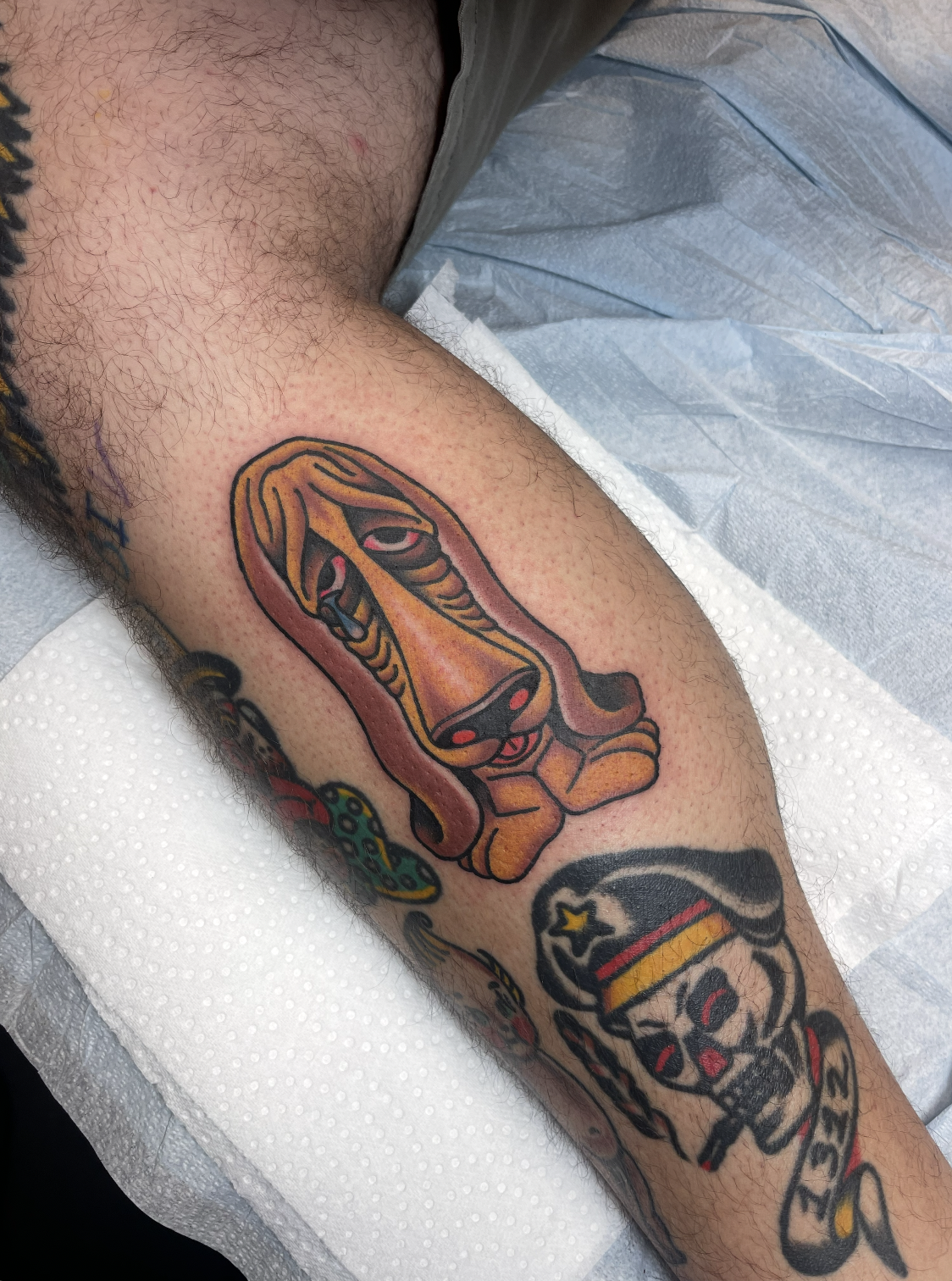 Tattoo of a stylized brown dog with elongated features on a person's forearm.
