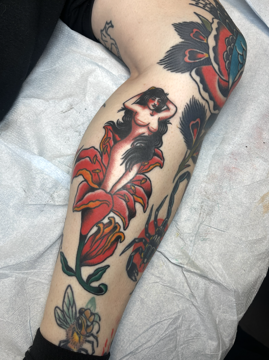 A tattoo of a nude woman with long dark hair, sitting on a large red flower, on a person's thigh.