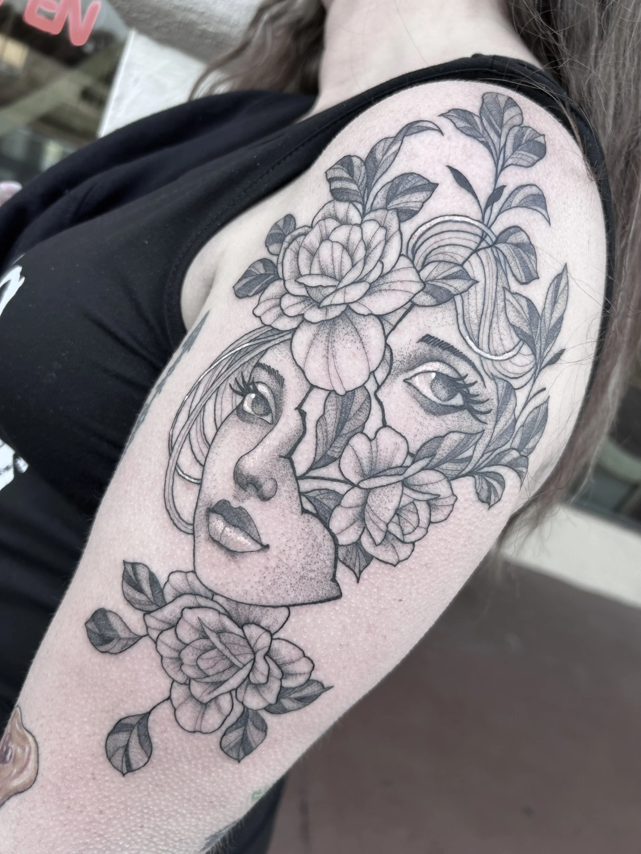Black and gray floral tattoo featuring large roses and leaves on a person's upper arm.