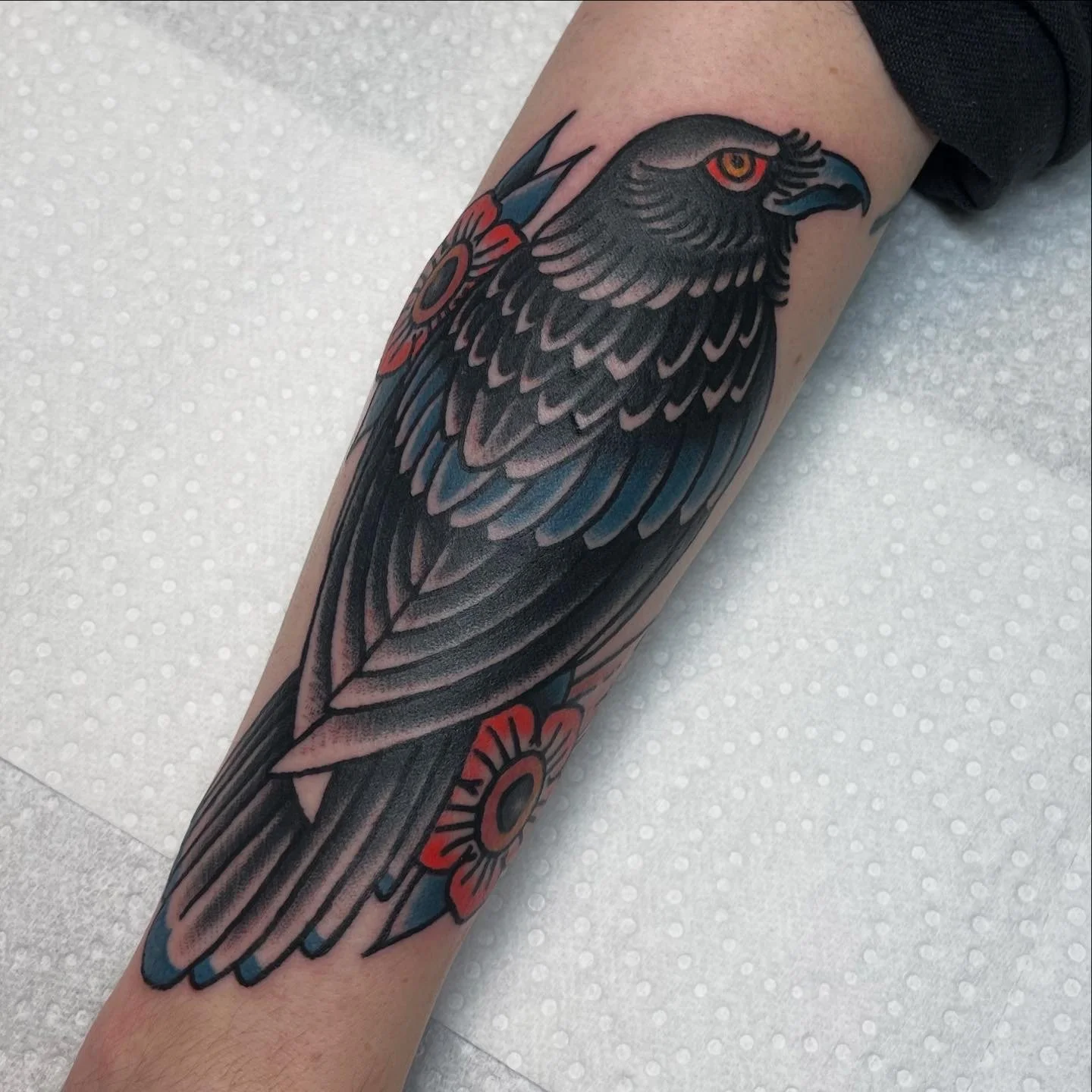 Tattoo of a bird's head with a fierce expression, detailed feathers, and colorful accents on the arm.
