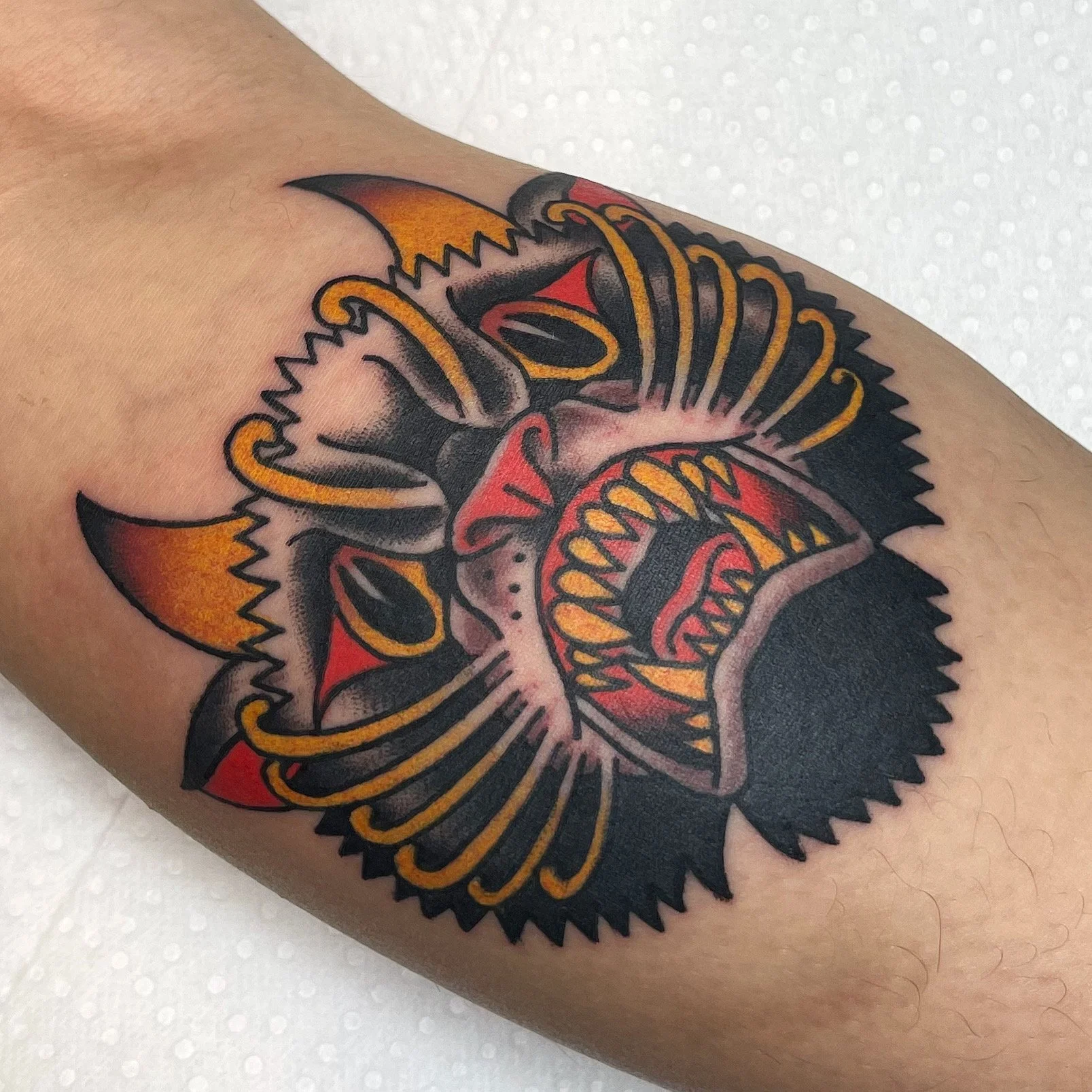 Colorful tattoo of a fierce tiger with sharp teeth, orange and black stripes, and black and red accents on the arm.