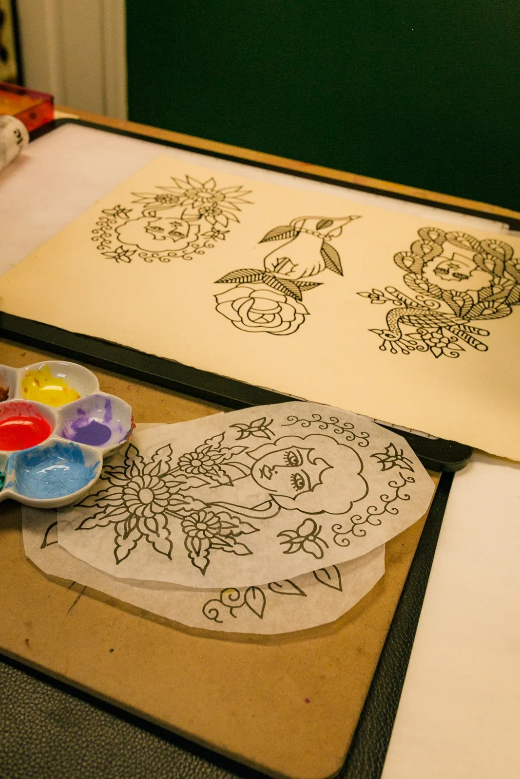 Coloring pages with floral and girl designs on a table, with a palette of paints nearby.