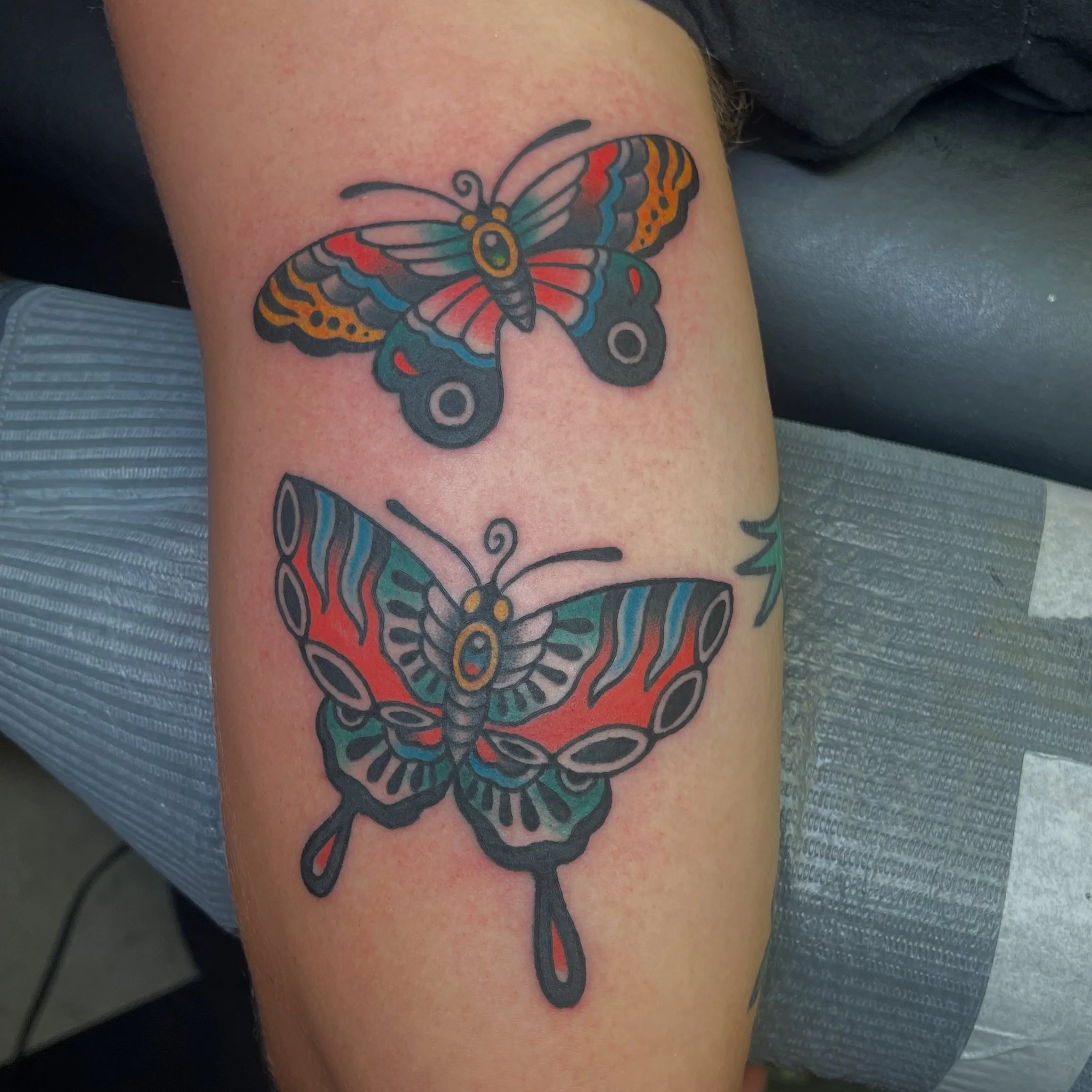 Colorful butterfly tattoo on person's arm, with black outline, red, yellow, blue, and orange wings.