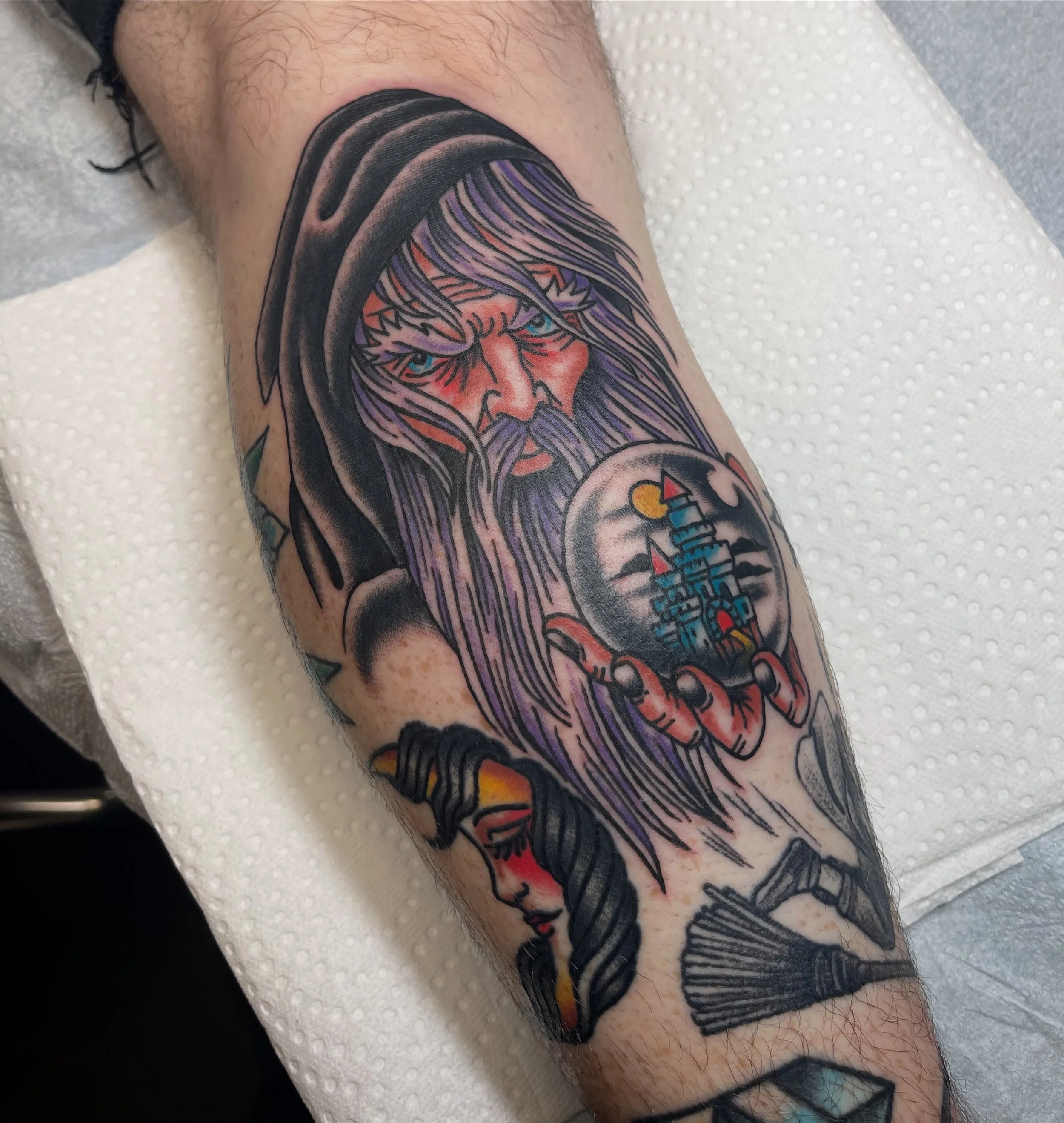 A colorful tattoo on a person's arm featuring a stylized face with long flowing hair, with elements of pastel and bright colors, and cartoonish details.
