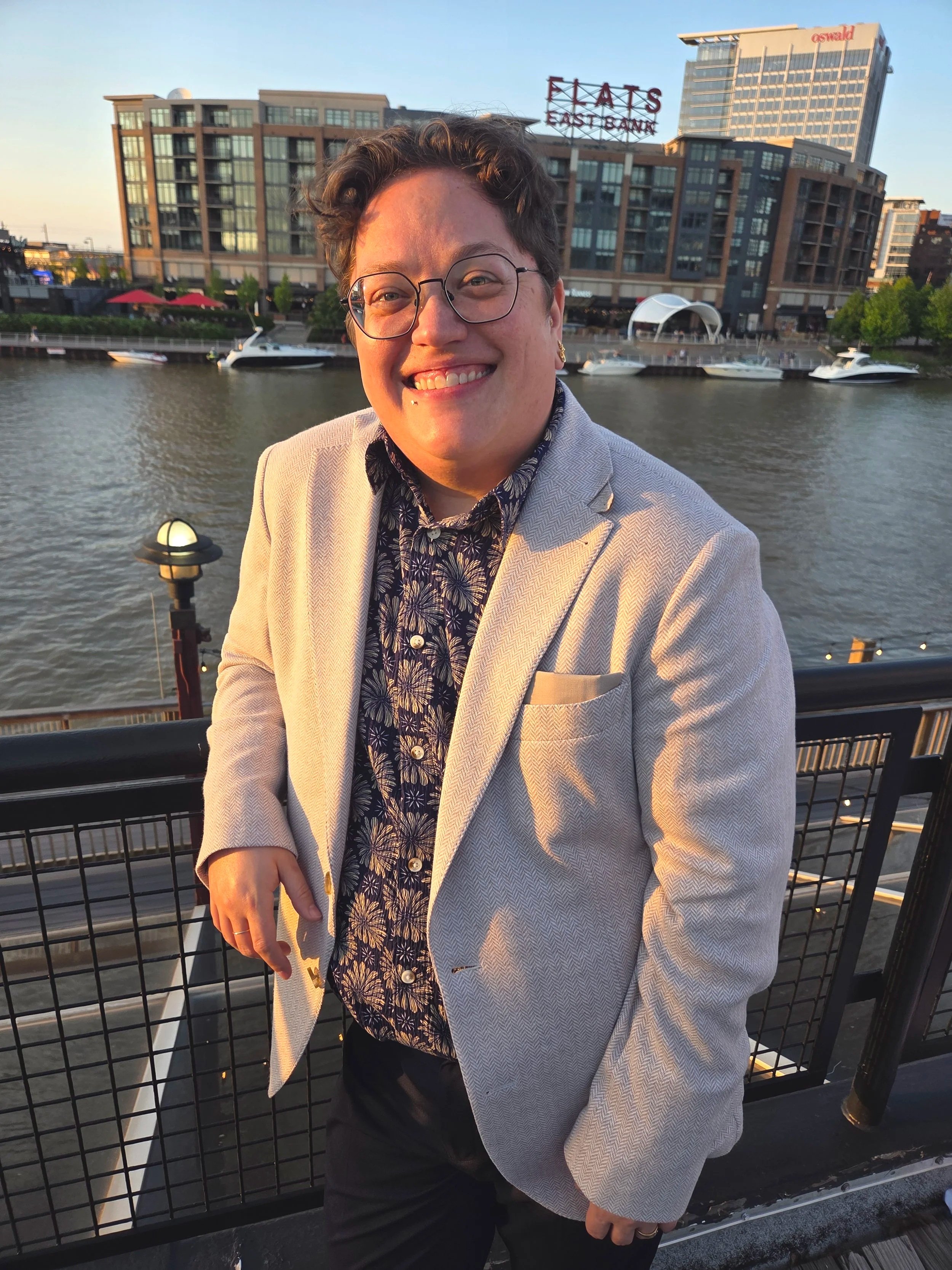 A photo of a queer, non-binary therapist standing in the West Bank of the Flats in Cleveland, Ohio.
