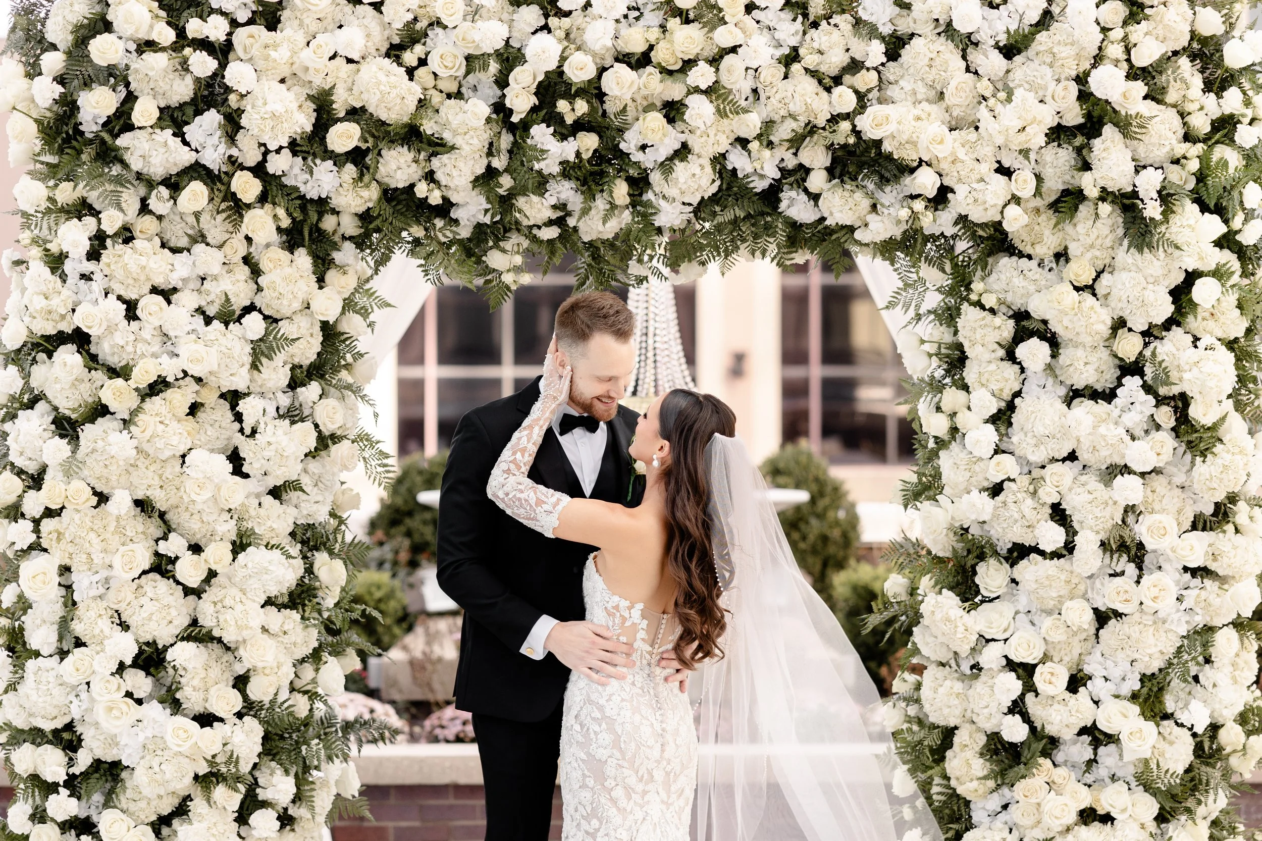 Bride and groom dancing under a custom white rose floral arch created by the in-house floral team at JPS Events at Regions Tower, downtown Indy's premier all-inclusive luxury rooftop wedding venue.