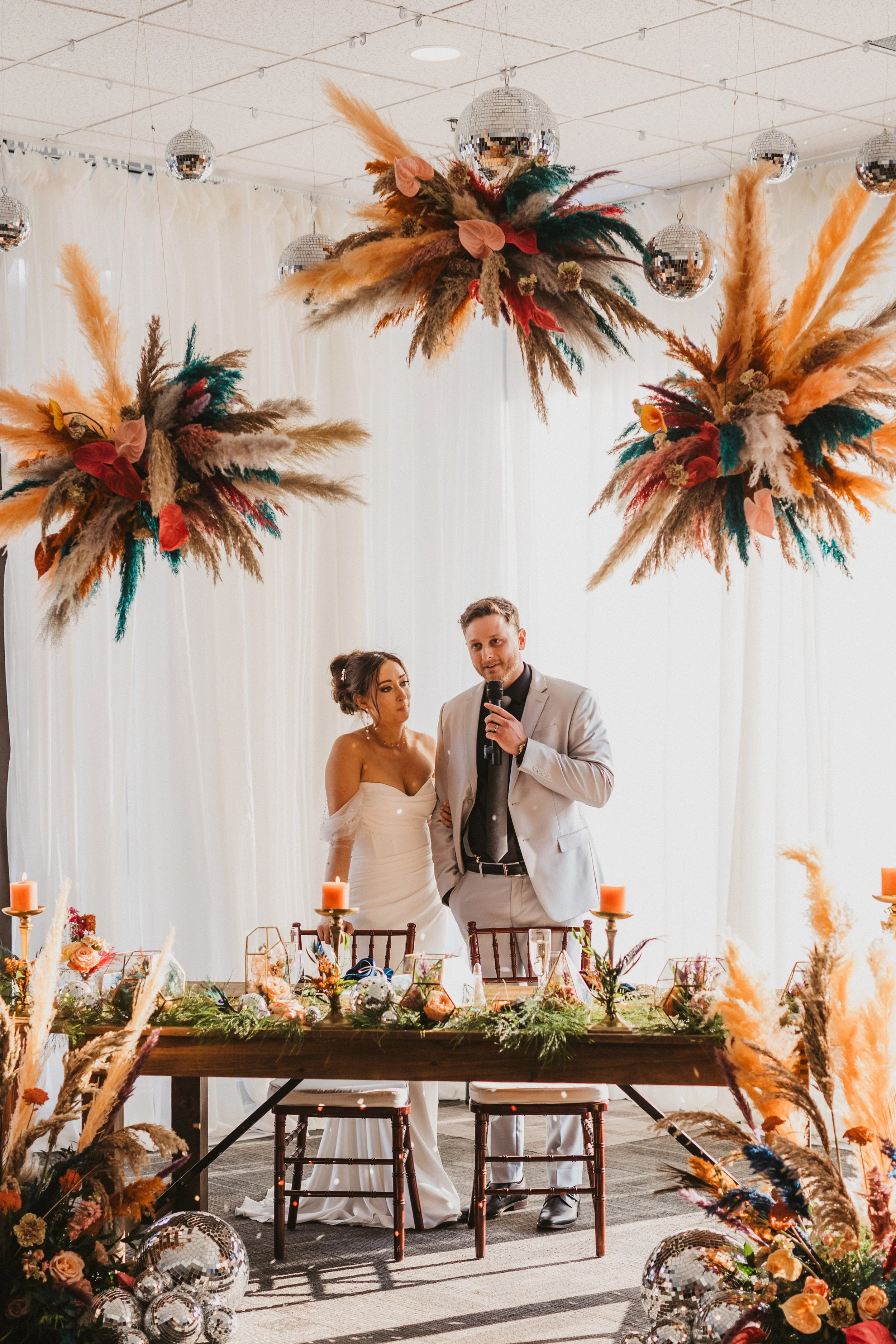 Couple at a modern chic sweetheart table at JPS Events at Regions Tower, featuring custom hanging feather installation, disco ball decor, in-house floral design, and complete day-of wedding coordination in downtown Indy.