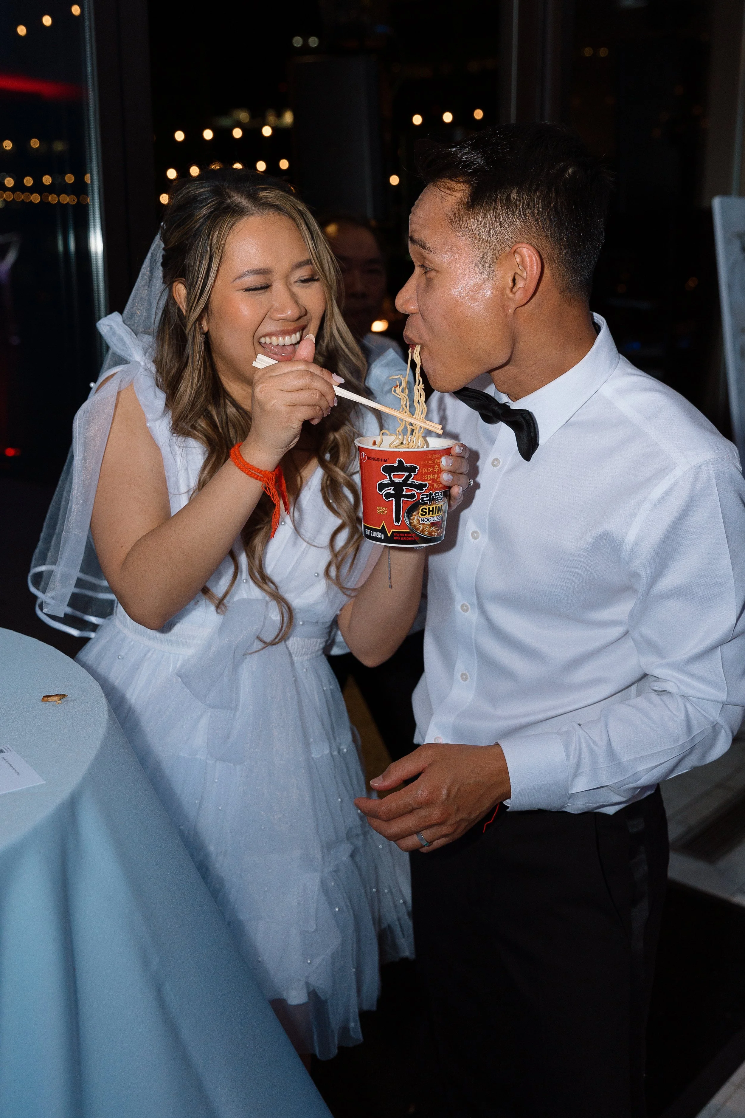 A bride and groom share late-night ramen noodles—an imaginative take on wedding late night snacks by JPS Events at Regions Tower in Downtown Indy. Nighttime city lights shine through floor-to-ceiling windows in our 5th-floor luxury ballroom.  
