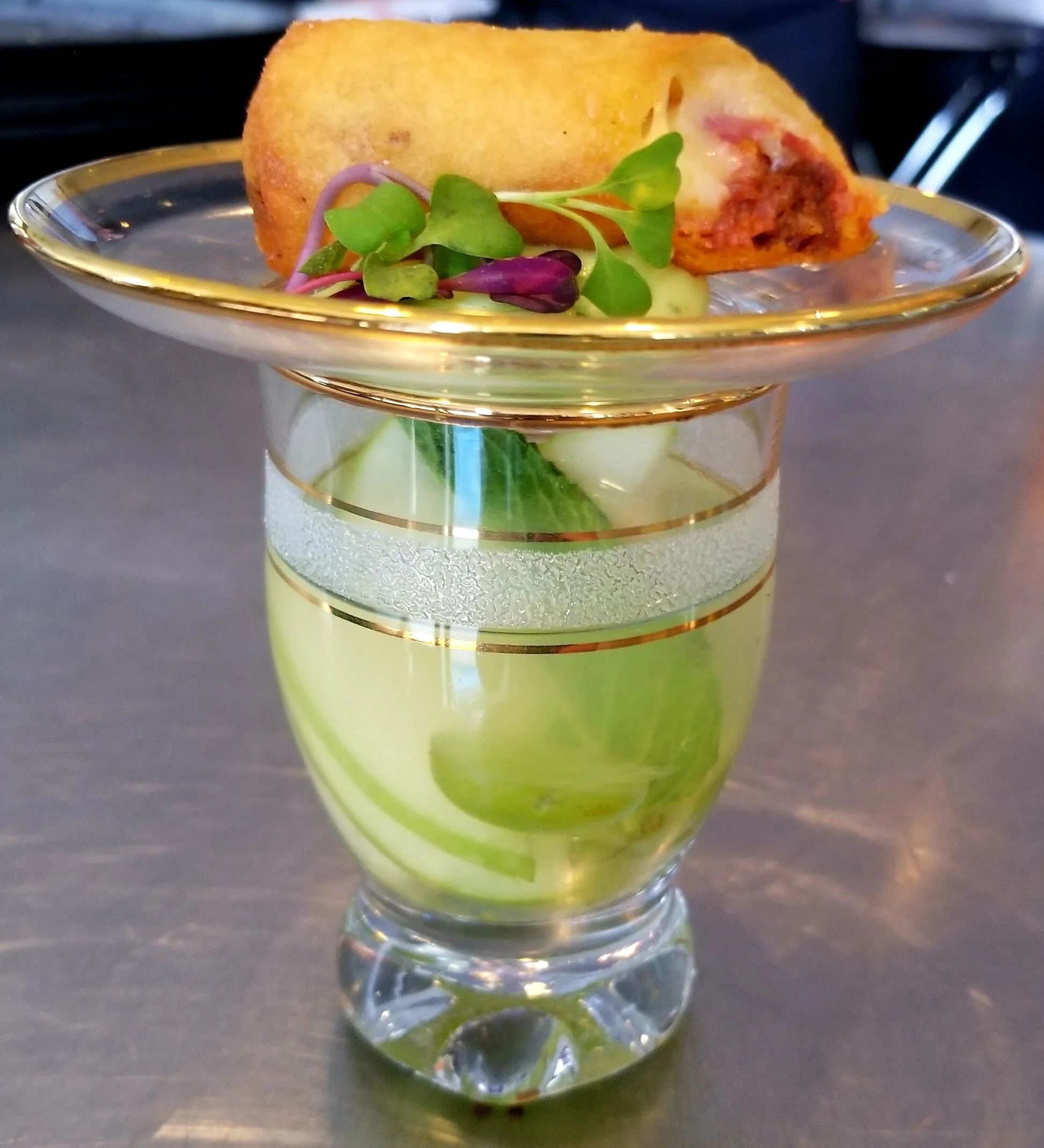 Dessert dish with a slice of cake in a glass cup, garnished with microgreens, on a black surface.