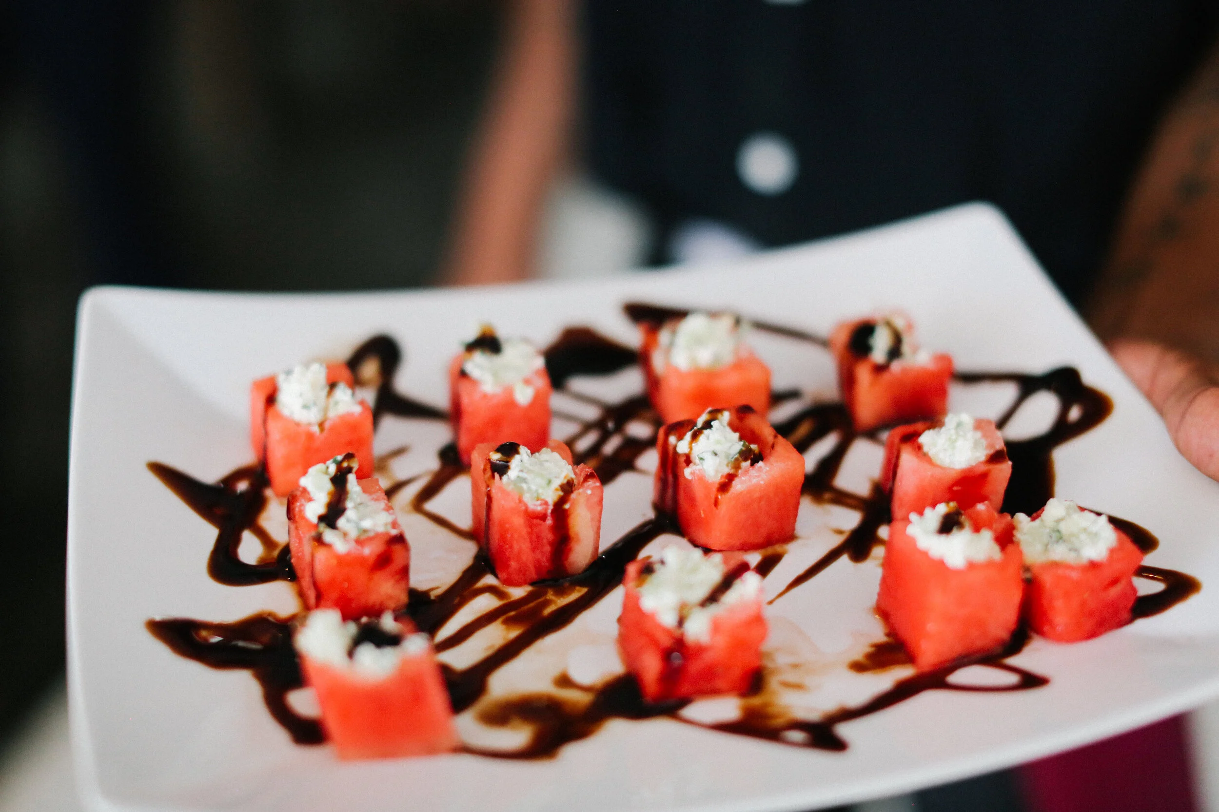 Chef-curated bespoke menus at JPS Events at Regions Tower in Downtown Indy: a white plate featuring rectangular slices of watermelon topped with ricotta cheese and balsomic for custom wedding menu selections.