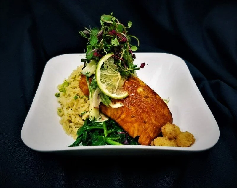 A plated meal from our luxury in-house catering at JPS Events at Regions Tower in Downtown Indianapolis, featuring grilled salmon, yellow rice, sautéed spinach, fresh greens salad, and savory bites on a white square plate.