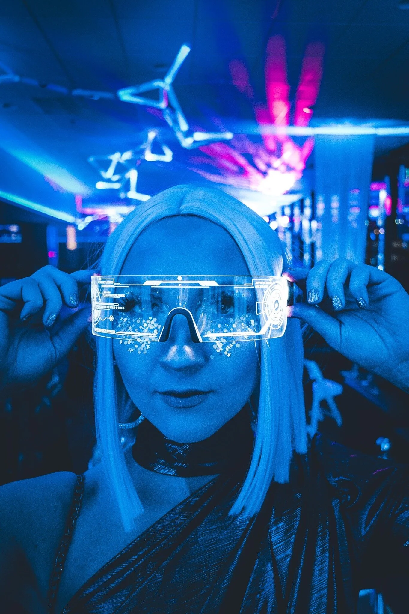 Person with platinum blonde hair holding futuristic transparent visor at HOT NYE (formerly CÎROC the New Year) at JPS Events at Regions Tower in Downtown Indy, in a neon-lit environment with colorful blue and purple lighting.  