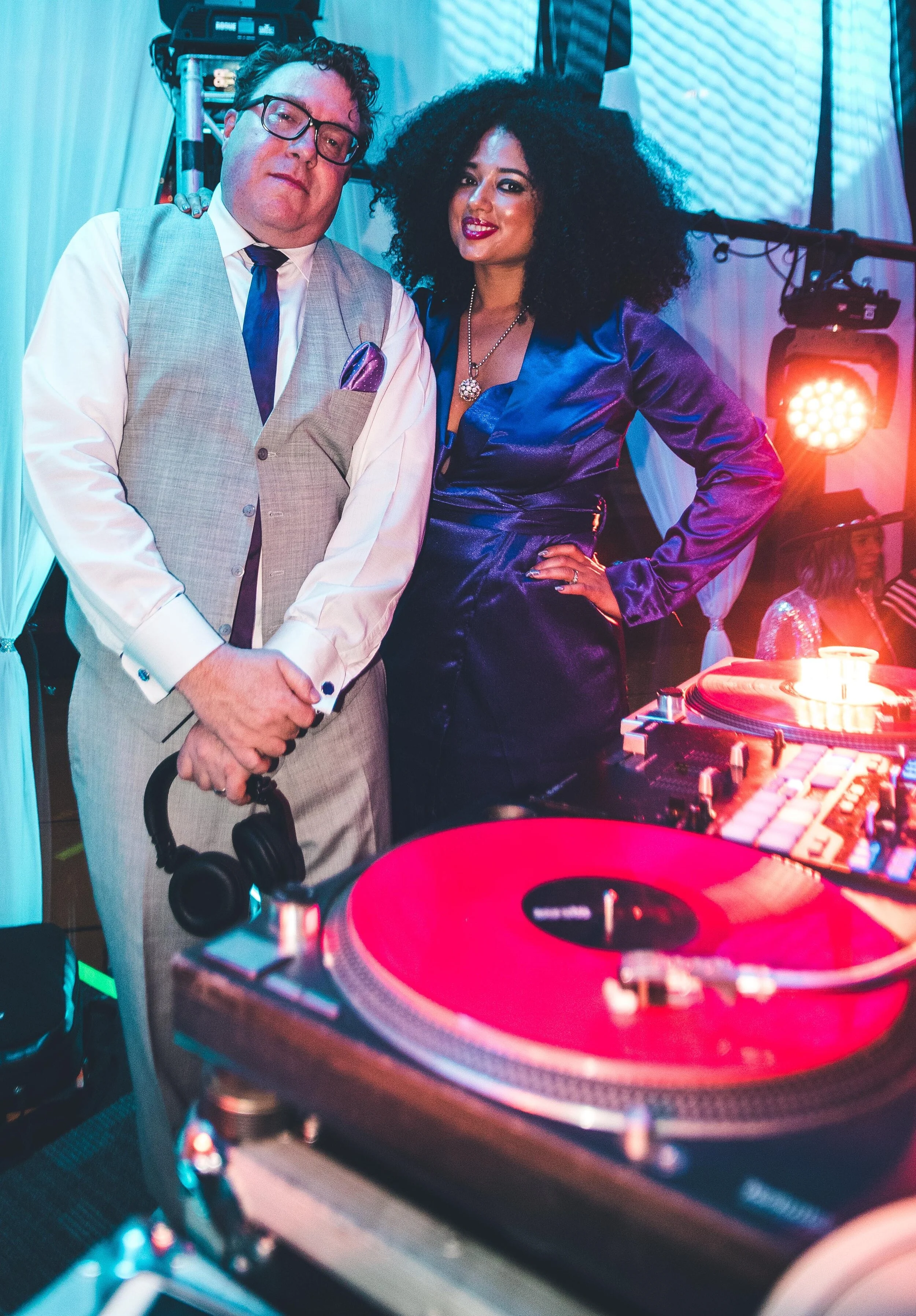 Two people, a man and a woman, DJ Indiana Jones and DJ Gabby Love, at HOT NYE (CÎROC the New Year) at JPS Events at Regions Tower in Downtown Indy, with DJ equipment and colored lights, smiling for the camera.  