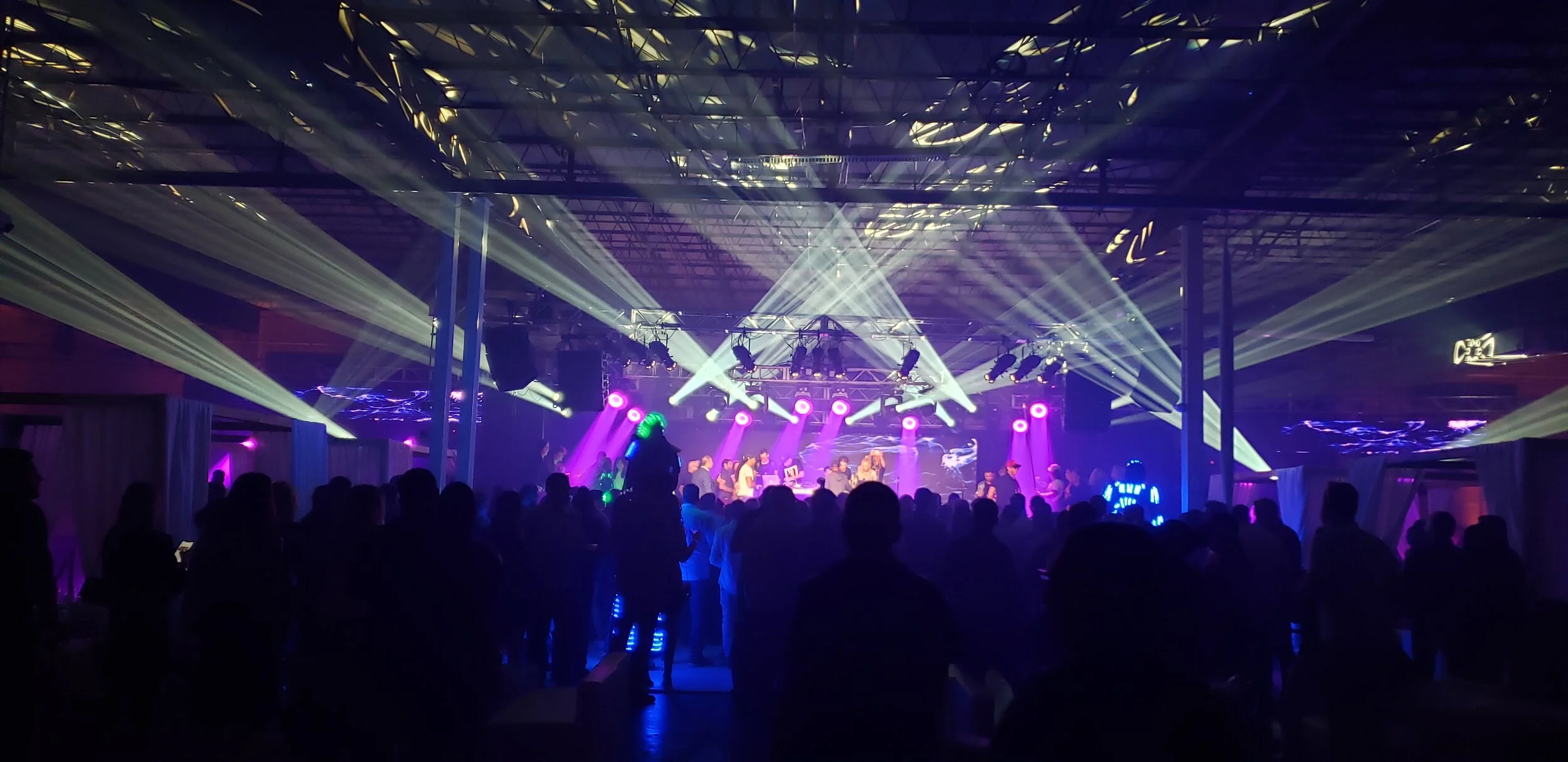 A lively nightclub scene produced by JPS Events for the LA Rams Super Bowl after party in Atlanta, featuring crowds dancing under bright laser lights, exposed beams, and large speakers at this premier luxury event.