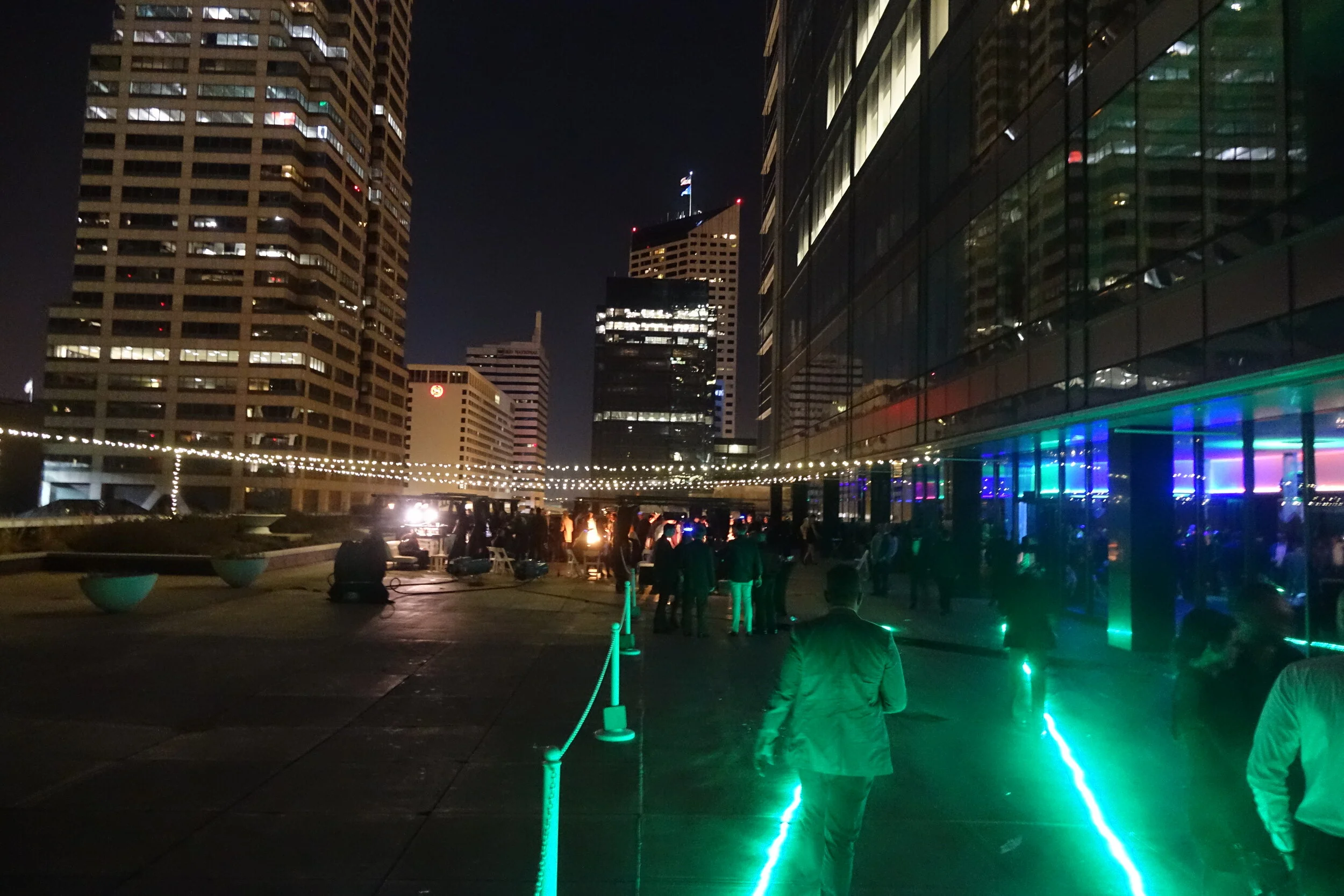 Nighttime cityscape with tall buildings, illuminated windows, and an outdoor gathering with string lights and colorful LED lighting at HOT NYE (formerly CÎROC the New Year) at JPS Events at Regions Tower terrace in Downtown Indy.