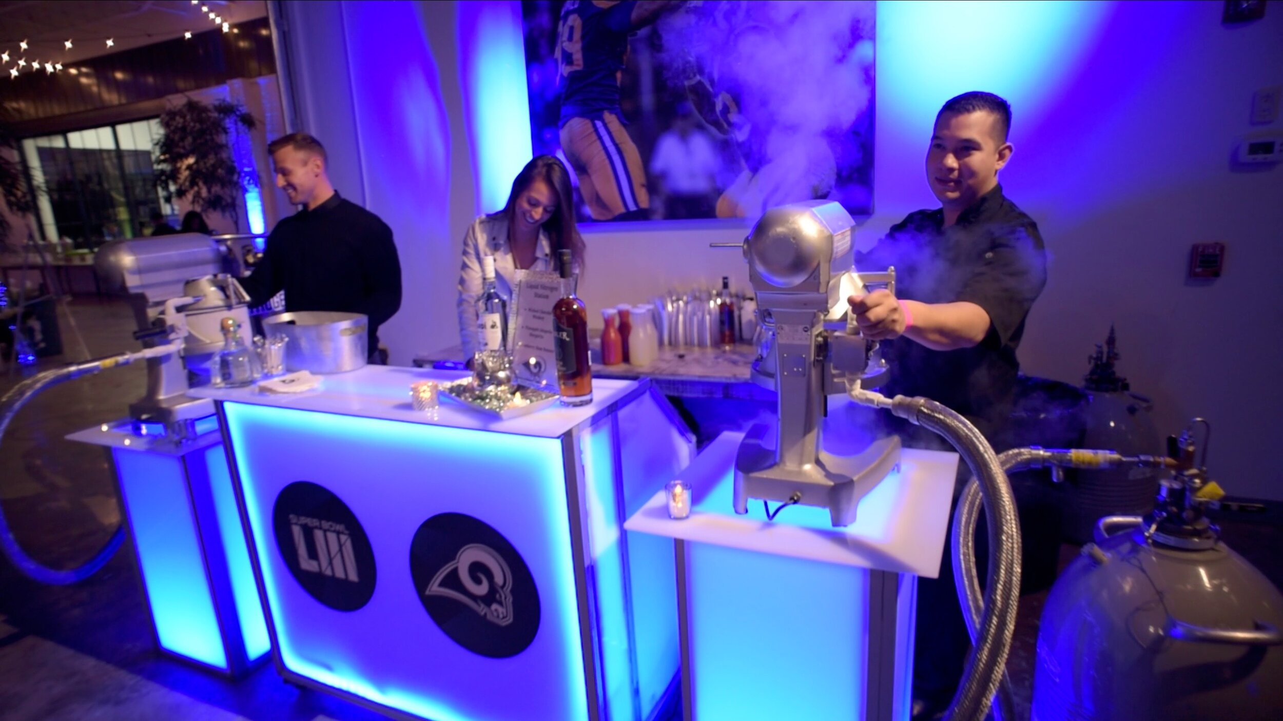People at a flash freeze nitrogen ice cream station with blue lighting, pipes, and bottles on the counter at the LA Rams Super Bowl after party produced by the full-service event team at JPS Events at Regions Tower.  