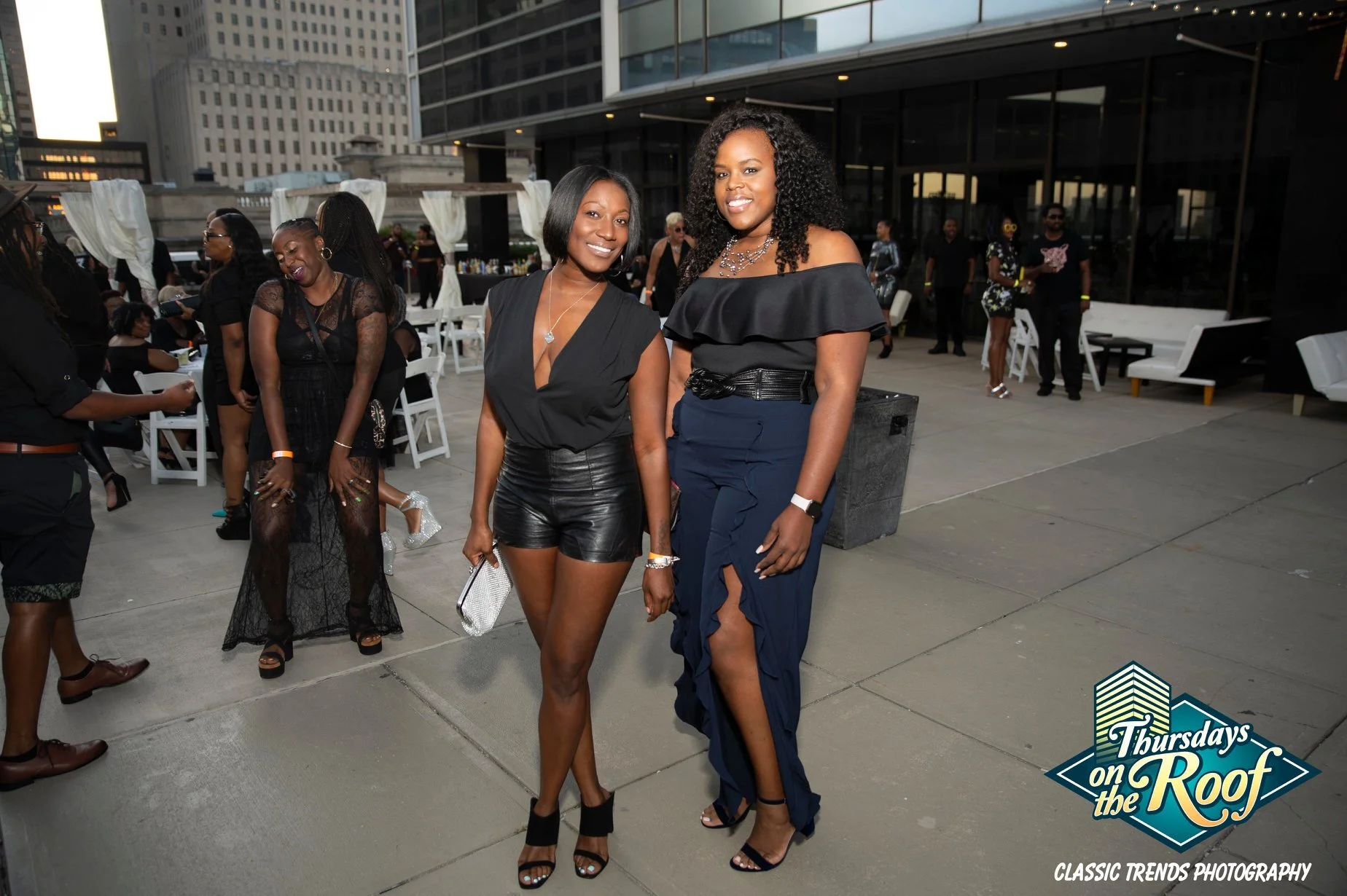 Two women posing at an outdoor rooftop event during Thursdays on the Roof on the 5th floor terrace at JPS Events at Regions Tower in Downtown Indy. Guests socialize near white draped cabanas at this iconic nightlife venue.  