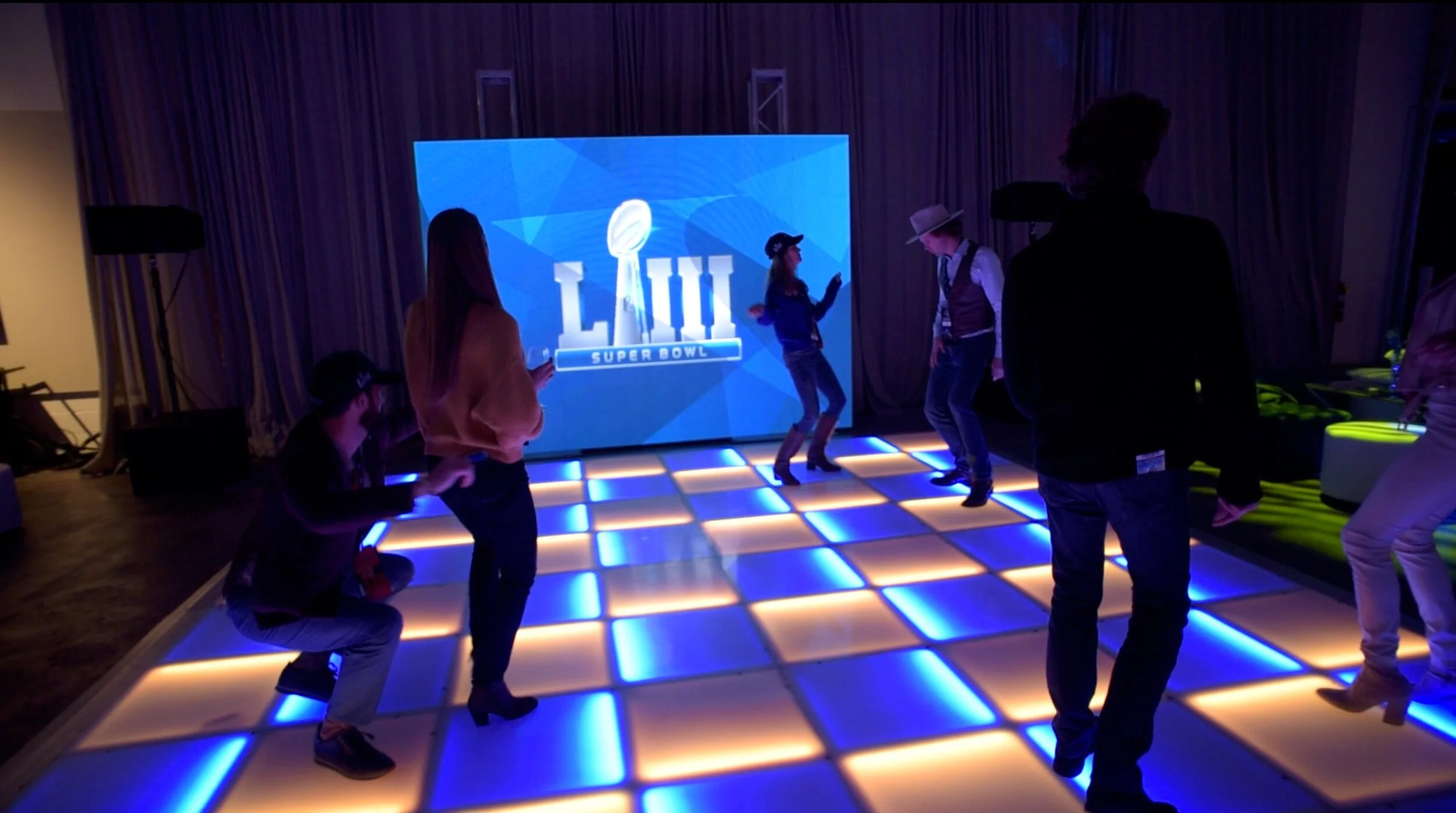 People dancing on an illuminated dance floor at the LA Rams Super Bowl after party produced by JPS Events, featuring a large screen displaying the Super Bowl logo in the background during this luxury event production.  