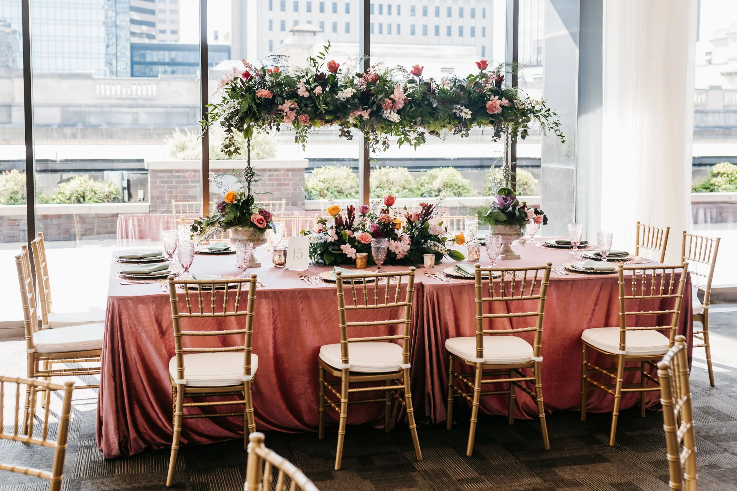 Mauve wedding tablescape at JPS Events at Regions Tower, featuring gold Chiavari chairs & an over-the-top hanging floral installation by our in-house florists at wholesale pricing, paired with chef-driven catering in downtown Indy.