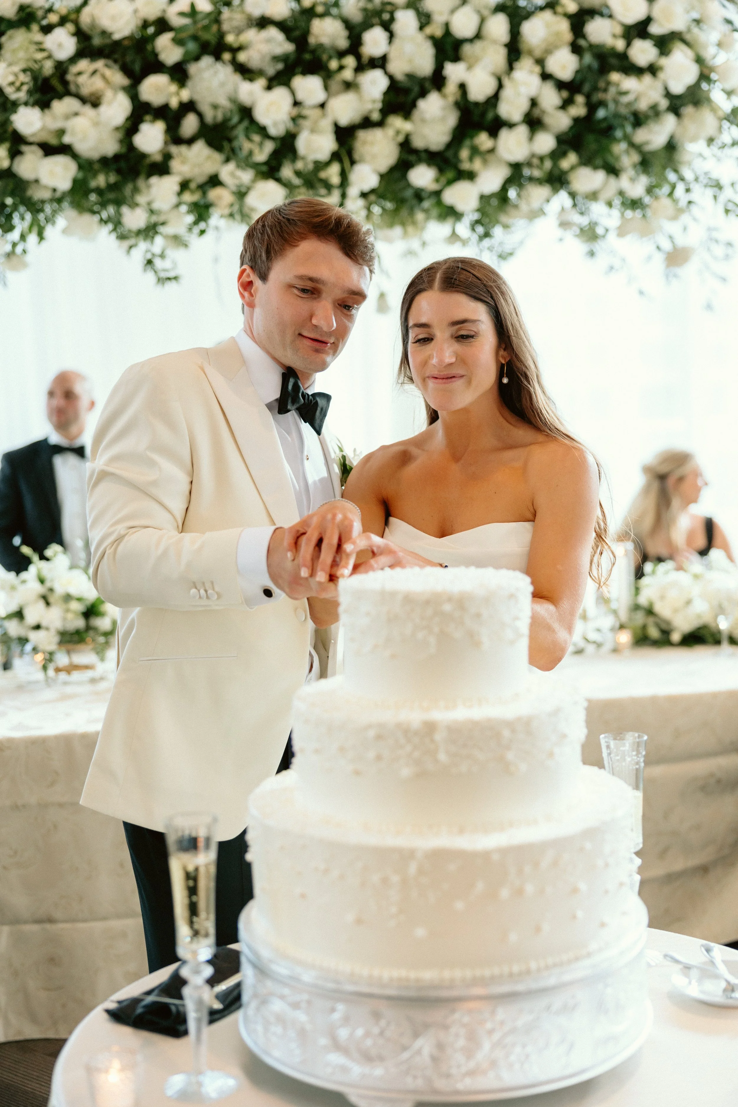 Bride & groom cutting cake under a white rose floral display at JPS Events at Regions Tower. Highlights chef-driven in-house catering, wholesale floral pricing, & all-inclusive wedding coordination in downtown Indy.