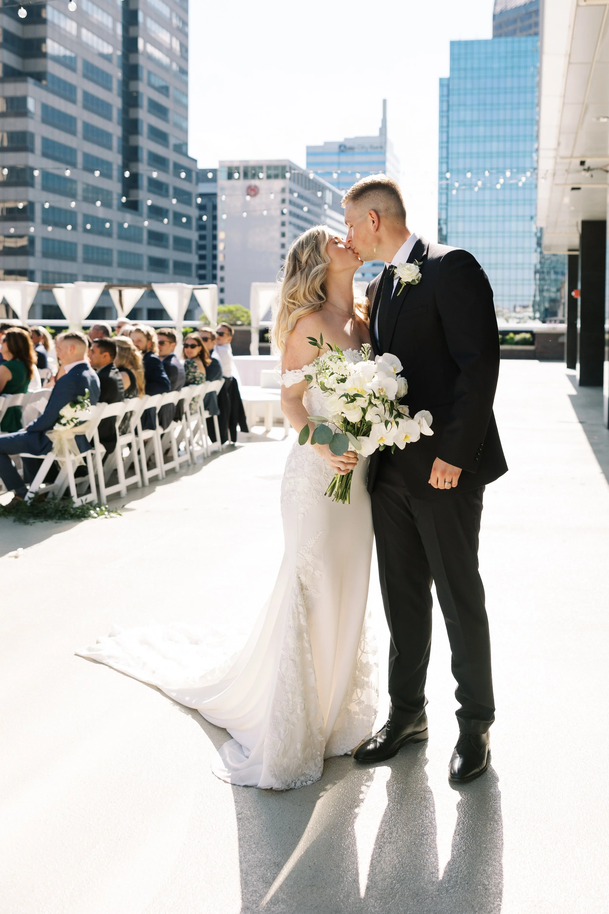 Newlyweds kissing at an outdoor ceremony on the 11,000 sq ft 5th-floor penthouse terrace at JPS Events at Regions Tower in downtown Indy. Features 360 skyline views, built-in coordination, & 6 walkable hotels.