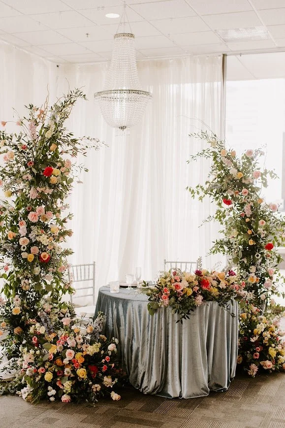 Weather-proof indoor ballroom wedding setup at JPS Events at Regions Tower, featuring custom in-house floral arches, polished white marble floors, chandeliers, and seamless all-inclusive planning in downtown Indianapolis.