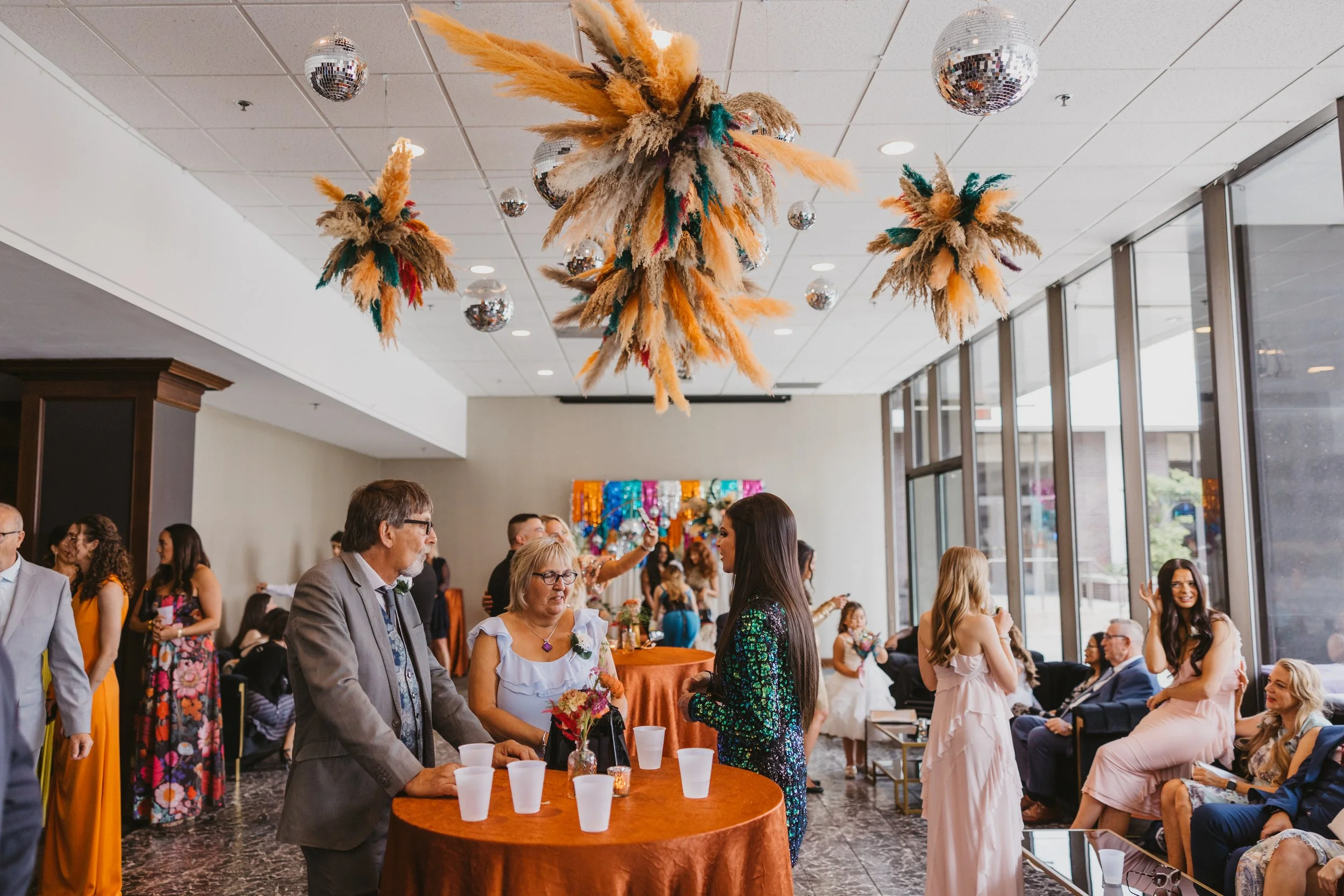 Indoor celebration with disco balls and colorful hanging decorations, with guests mingling and sitting at tables.