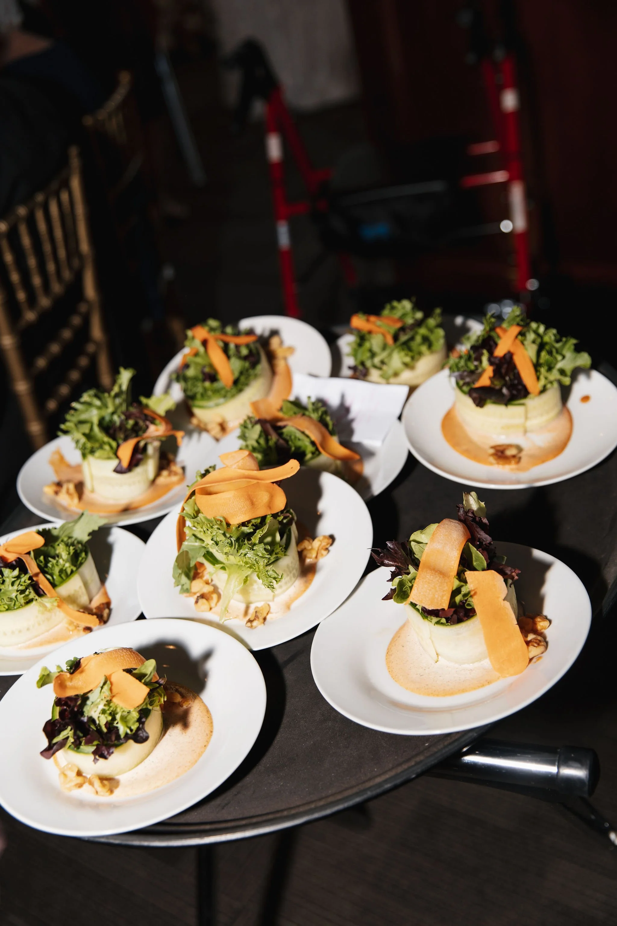 Multiple plated salads topped with mixed greens and shredded carrots, arranged on a black surface.