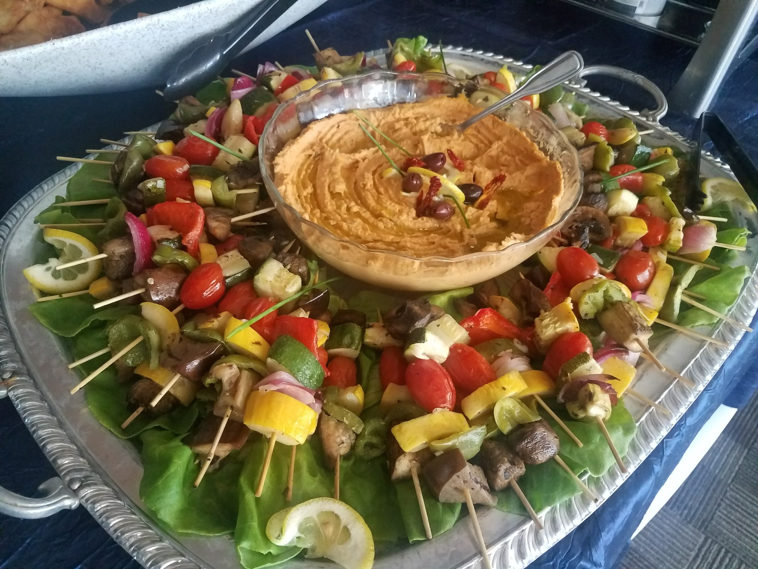 A large silver tray filled with colorful vegetable skewers surrounding a bowl of hummus, garnished with olives, red pepper, and lemon slices from luxury in-house catering at JPS Events at Regions Tower in Downtown Indianapolis.