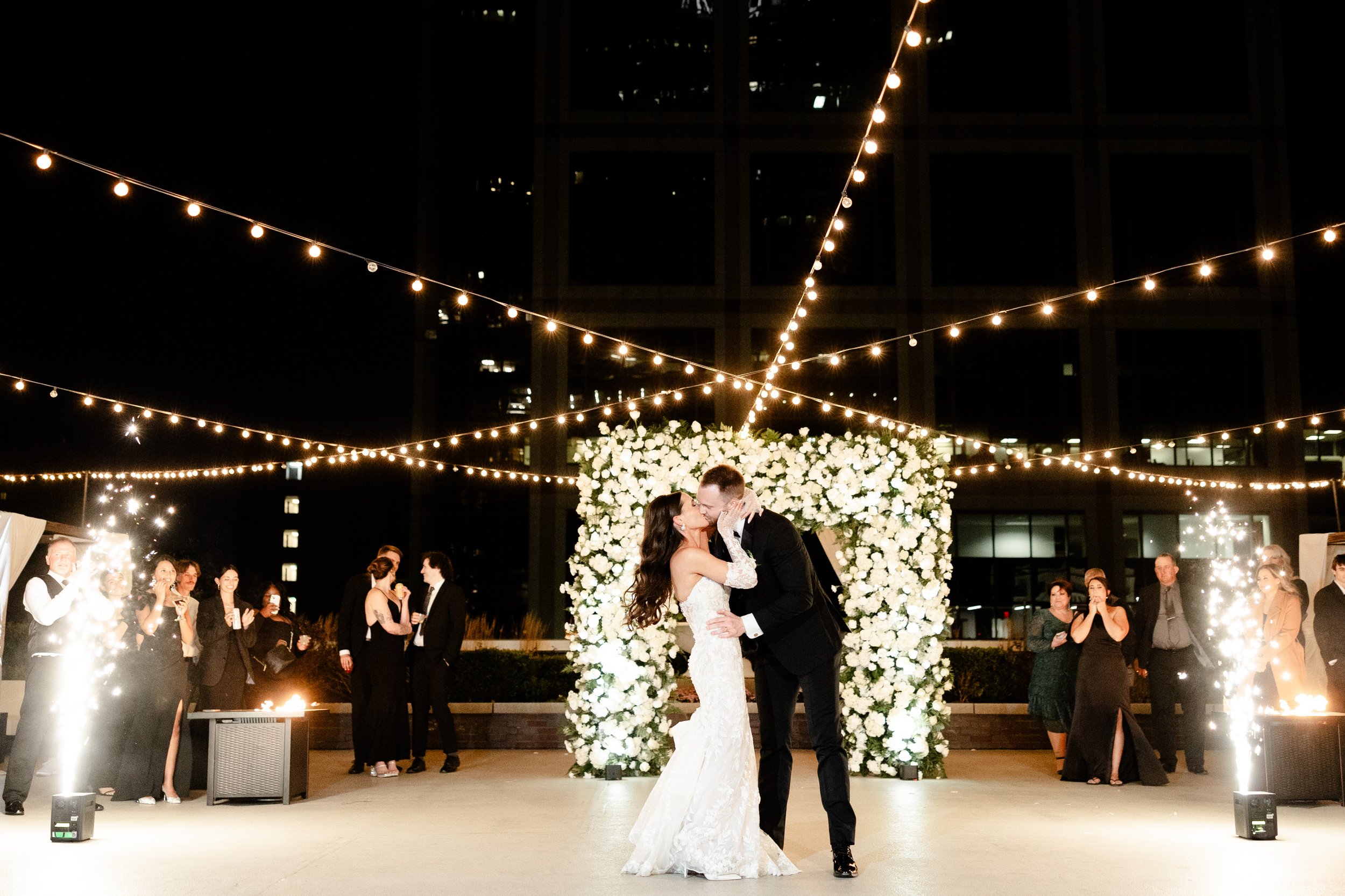Bride & groom kiss under string lights & cold spark fountains on the 11,000 sq ft terrace at JPS Events at Regions Tower. High-end night production, 360 Indy skyline views, & zero late-out fees.
