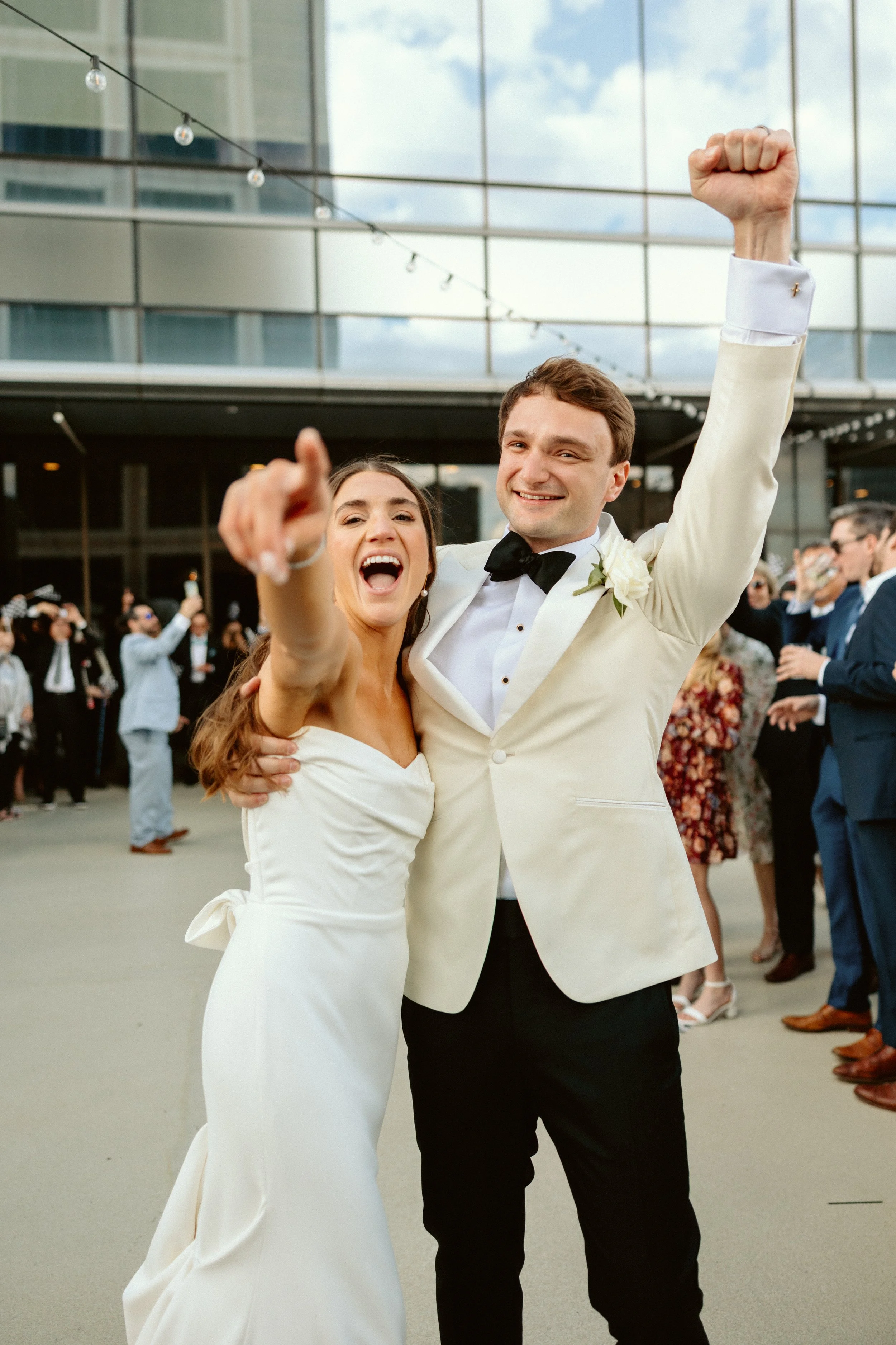 A couple in wedding attire celebrating outdoors with guests in the background.