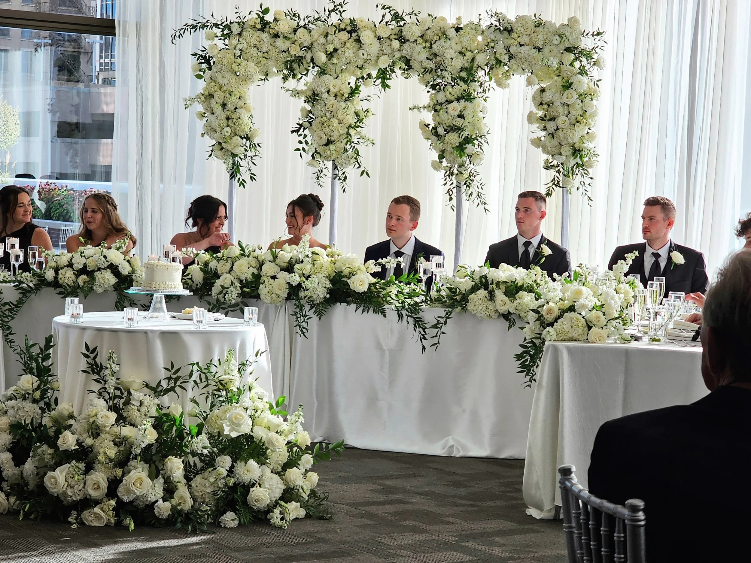 Head table reception setting at JPS Events at Regions Tower, featuring chef-driven in-house catering, bespoke white rose floral design, wedding cake presentation, and built-in day-of coordination in downtown Indy.