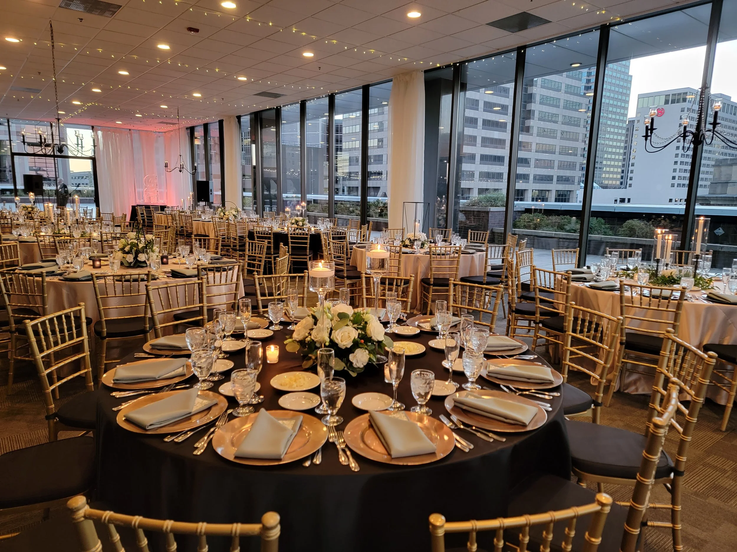 Corporate banquet setup in the indoor ballroom at JPS Events at Regions Tower, featuring in-house floral centerpieces, floor-to-ceiling windows, warm chandeliers, and all-inclusive planning in downtown Indy.
