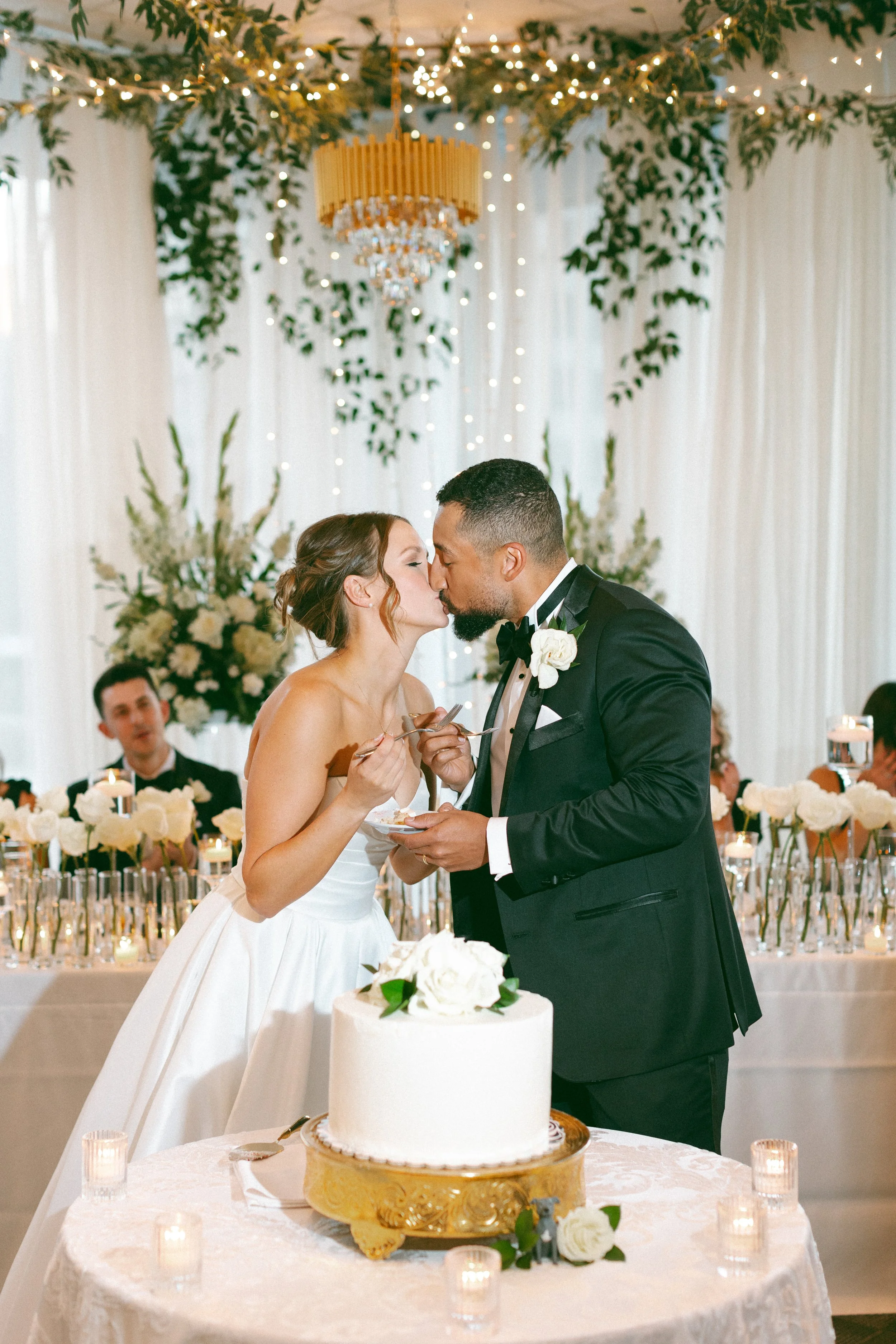 Bride & groom kiss during their wedding cake cutting reception at JPS Events at Regions Tower. Highlights chef-driven in-house catering, custom hanging florals at wholesale pricing, & full-service coordination in downtown Indy.
