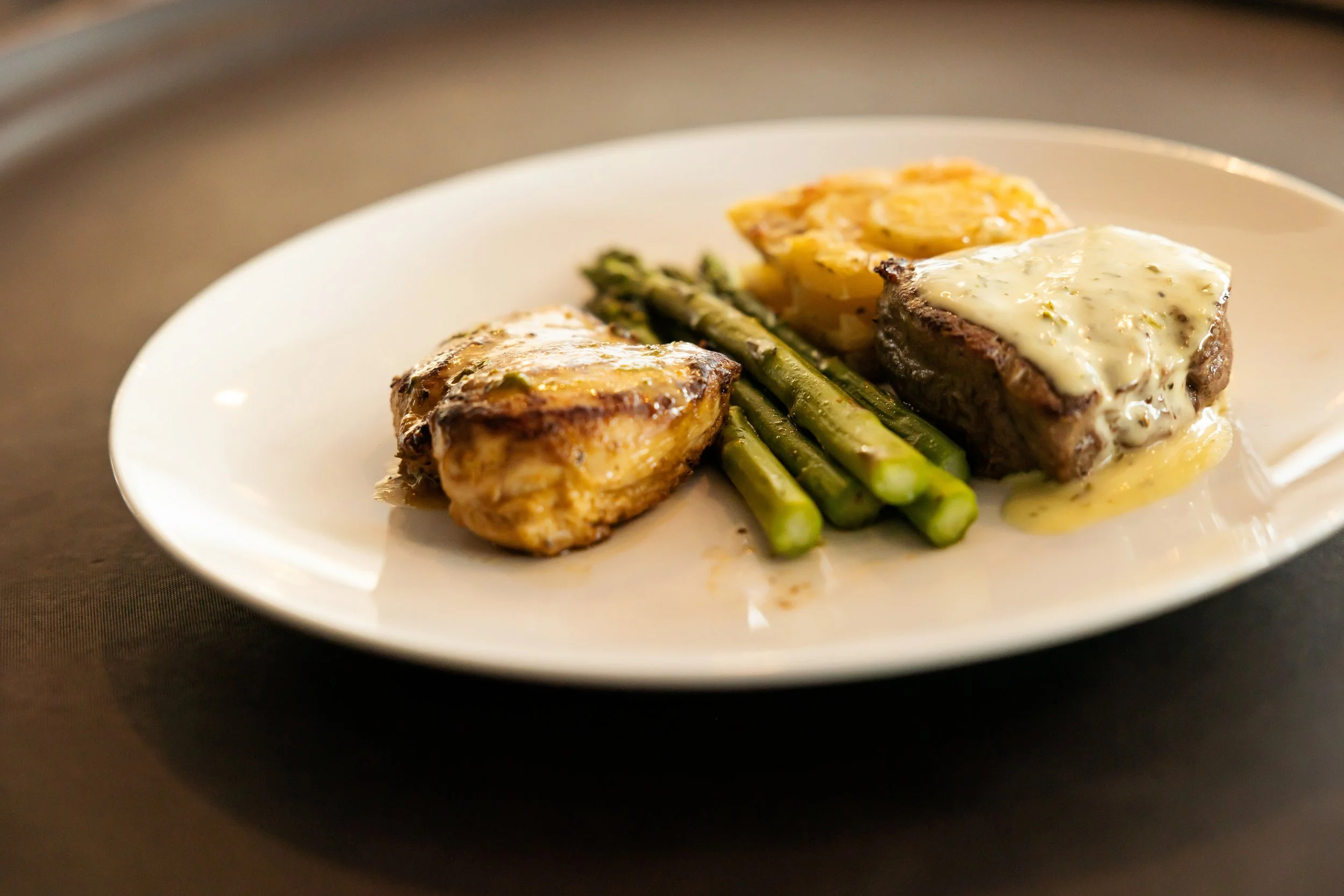 A plate of food with grilled chicken topped with creamy sauce, green asparagus, and roasted potatoes—chef curated bespoke menus from luxury in-house catering at JPS Events at Regions Tower in Downtown Indy.  
