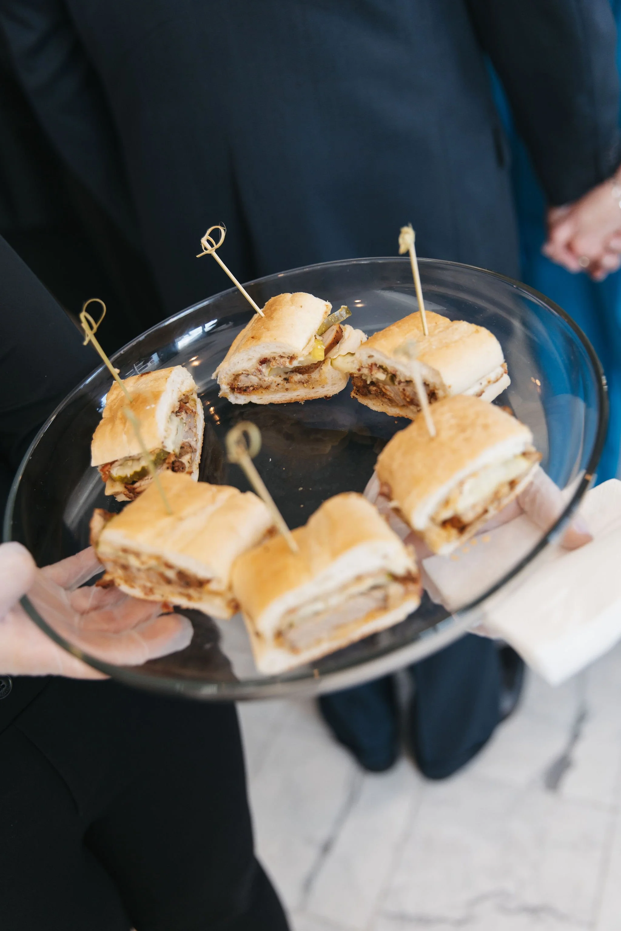A server holds a glass tray with sliced sandwich passed hors d'oeuvres secured with toothpicks at a formal wedding event hosted at JPS Events at Regions Tower in Downtown Indianapolis, catered by our luxury in-house culinary team.  