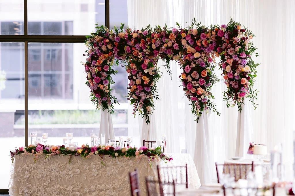 Custom pink and purple floral wedding arch designed by the in-house floral team at JPS Events at Regions Tower, offering wholesale pricing, all-inclusive decor, and floor-to-ceiling window views in downtown Indianapolis.