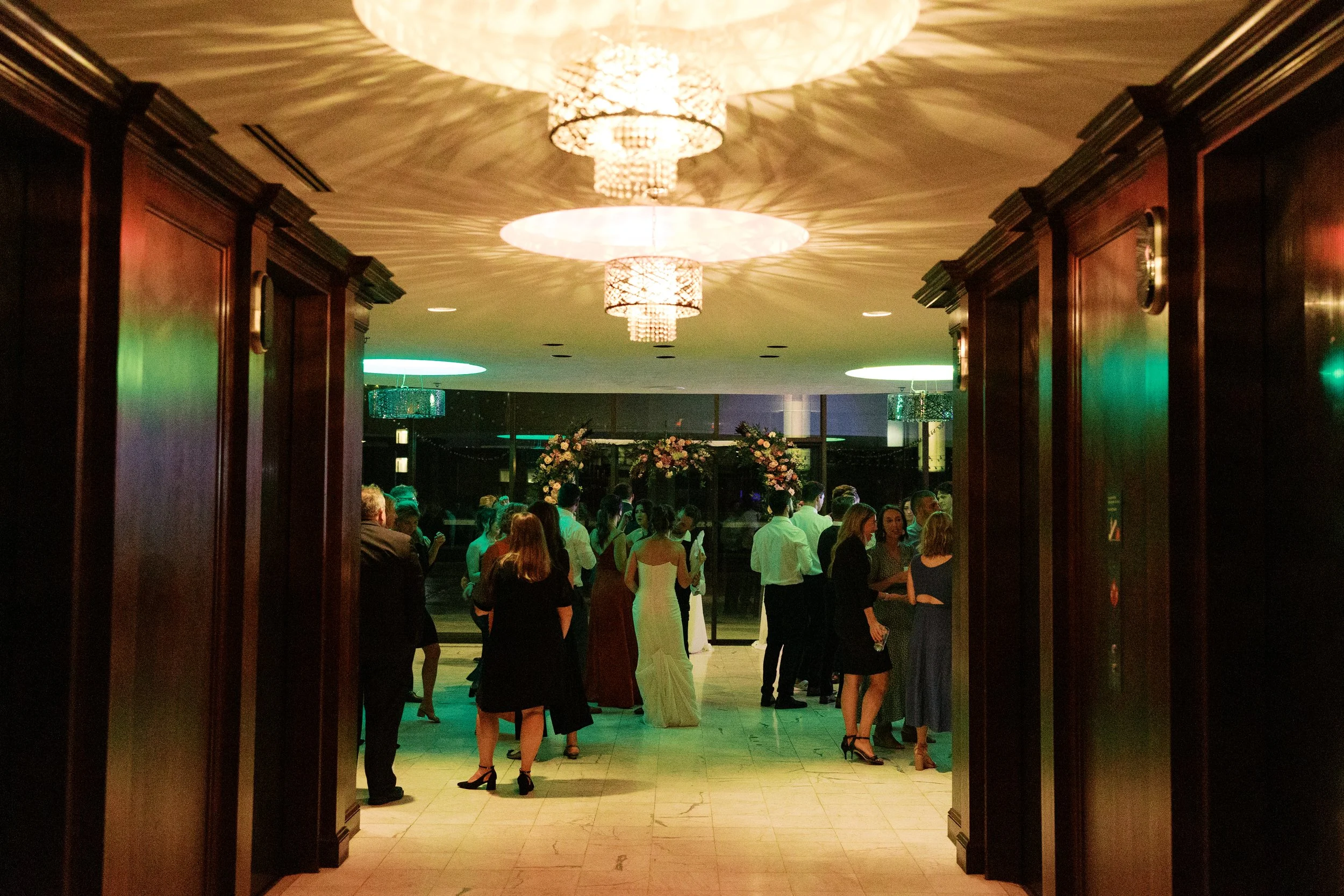 Weather-proof indoor ballroom wedding reception at JPS Events at Regions Tower. Features dark wood paneling, polished white marble floors, crystal chandeliers, & seamless indoor-outdoor terrace access in Indy.
