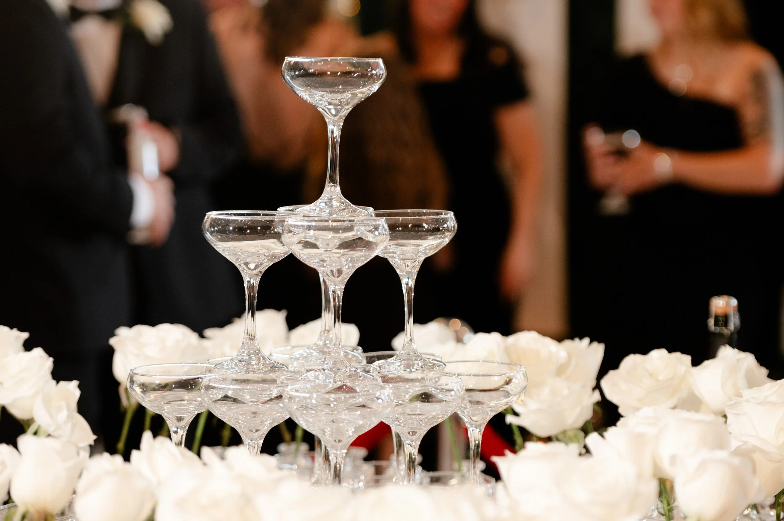 Tiered champagne tower glass pyramid on a white rose table at JPS Events at Regions Tower. Showcases our handcrafted in-house bar program, wholesale floral pricing, & chef-driven catering in downtown Indy.