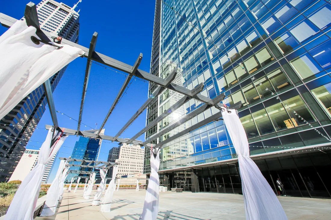 Outdoor cityscape with modern glass skyscraper buildings and a metal frame structure with white fabric hanging from it.