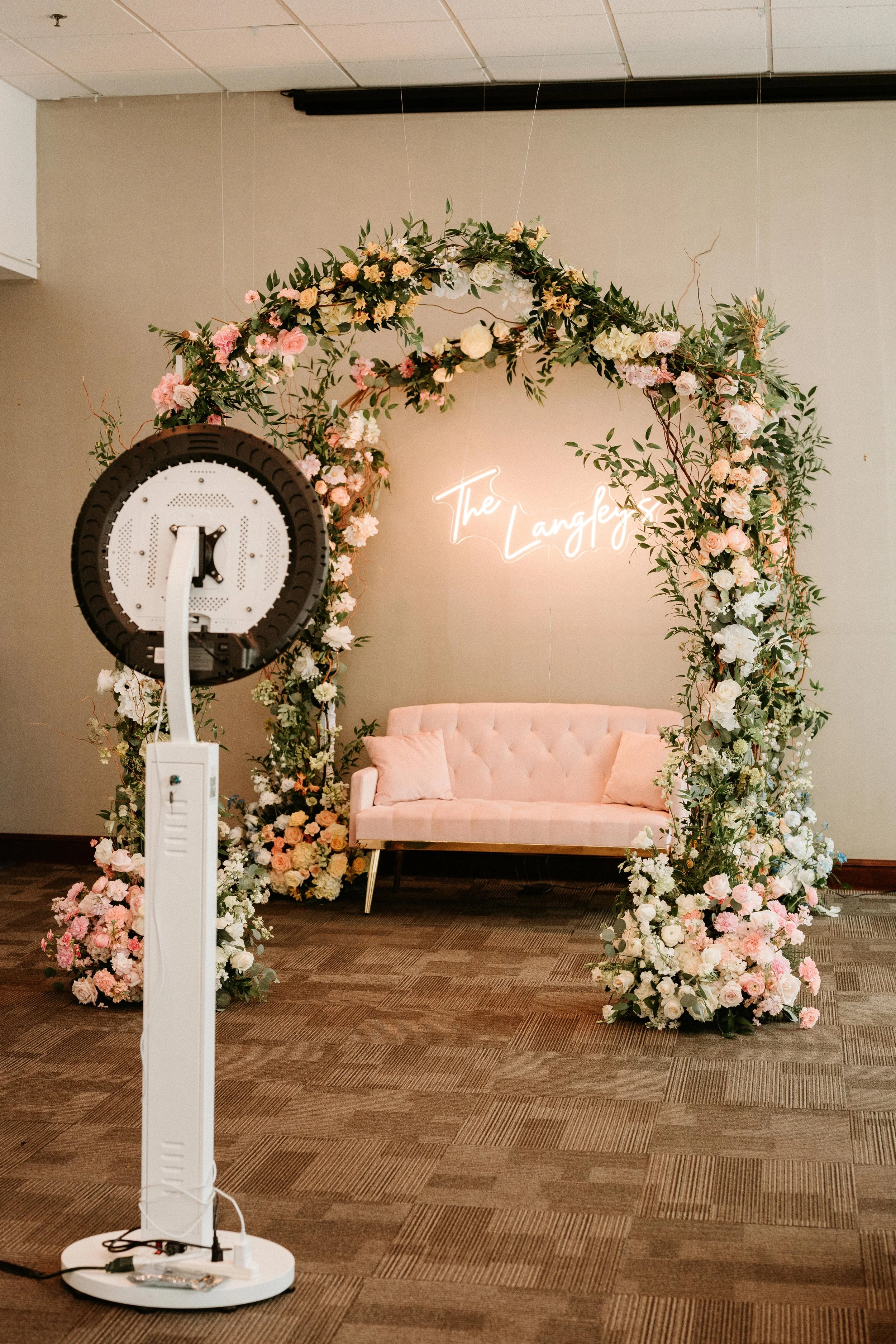 Custom neon sign lounge backdrop with a pink sofa & floral arch by JPS Events at Regions Tower. Features in-house decor, built-in photo booth activations, & all-inclusive design in downtown Indy.