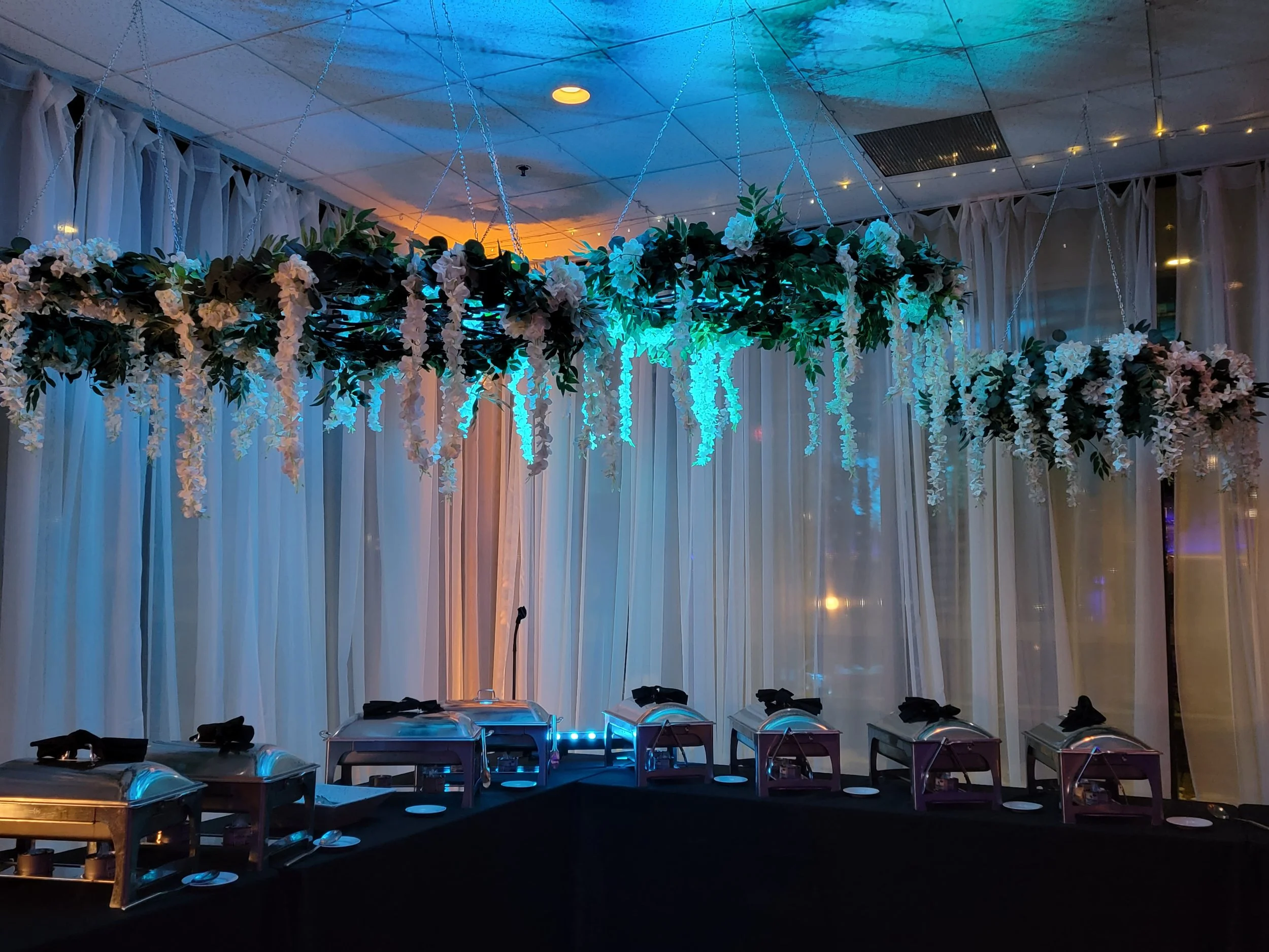 Chef-driven in-house catering buffet setup at JPS Events at Regions Tower, framed by custom overhead hanging floral installations and architectural lighting created by the in-house floral and production team.