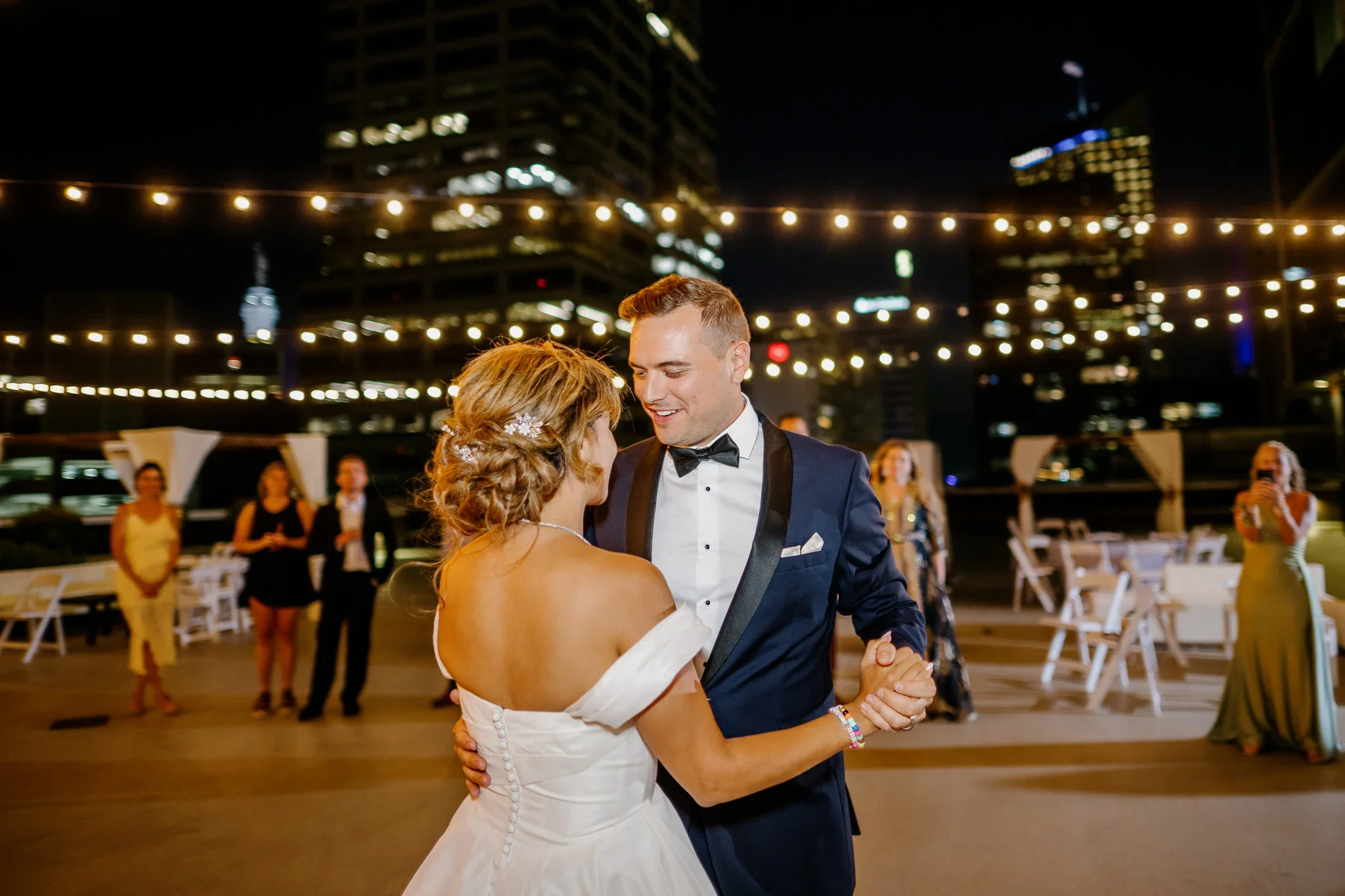 Newlyweds dance at night under string lights on the 11,000 sq ft 5th-floor rooftop terrace at JPS Events at Regions Tower, the largest private outdoor rooftop venue in Downtown Indianapolis featuring 360-degree skyline views.