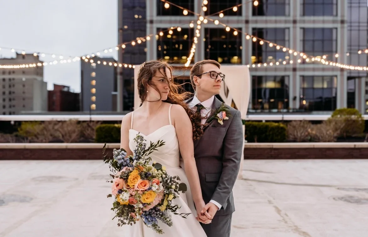 A newlywed couple holding hands on the 11,000 sq ft 5th-floor terrace—the largest private outdoor rooftop venue in Downtown Indianapolis—at JPS Events at Regions Tower during dusk, with 360-degree city skyline views in the background.