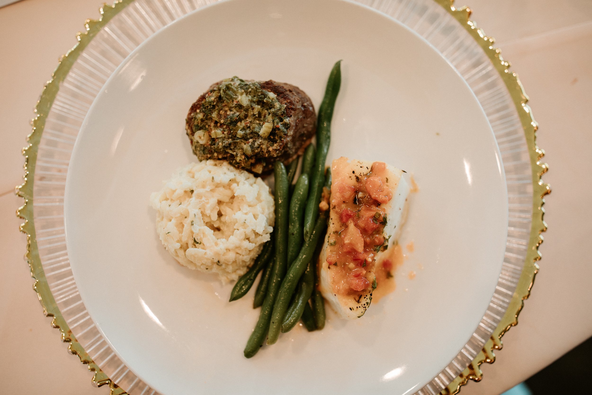 Seasonal selections from luxury in-house catering at JPS Events: plate featuring creamy risotto, green beans, a beef filet in gravy, and baked salmon with tomato on a gold-rimmed charger (one of many charger options available to rent at JPS Events)
