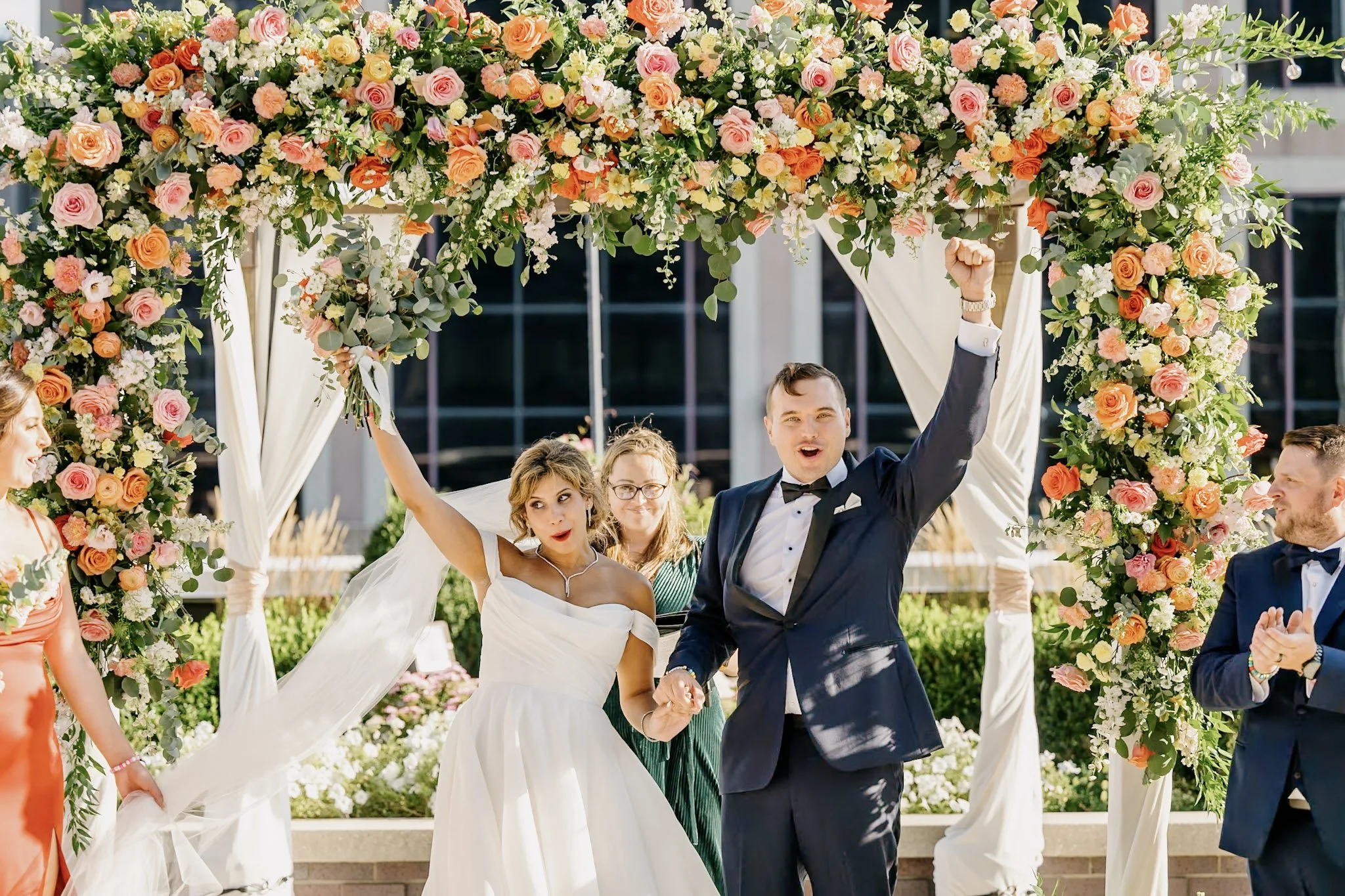 Bride and groom celebrating on the 11,000 sq ft 5th-floor penthouse terrace at JPS Events at Regions Tower under a custom colorful floral arch created by our in-house team, with 360 skyline views in downtown Indy.